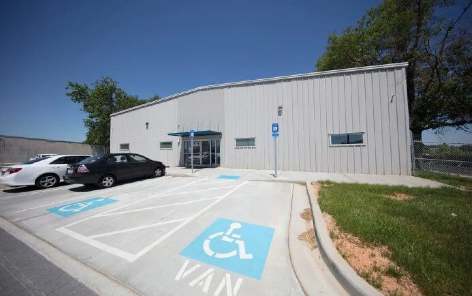 Accessible parking spaces in front of a modern industrial building with cars and clear blue sky.