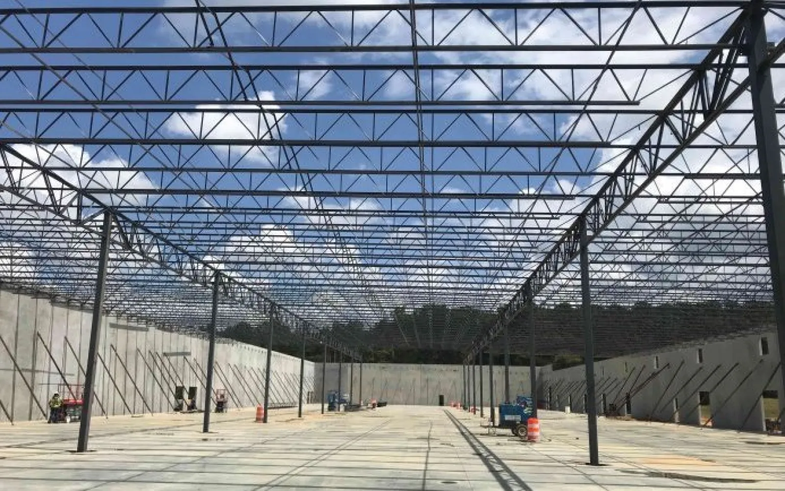 Steel framework and concrete walls of a large industrial building under construction with clear blue sky.