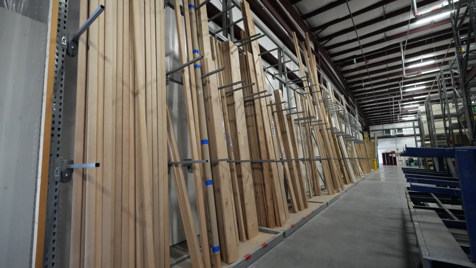 Rows of wooden planks neatly organized on metal racks inside a spacious warehouse with concrete floors.