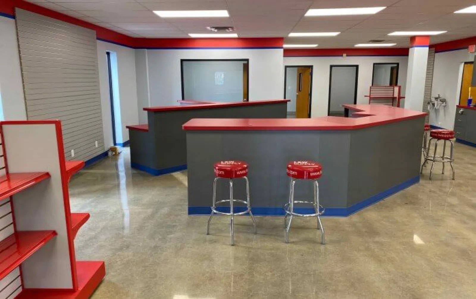 Modern commercial space with red and gray counters, stools, shelving, and polished concrete floor.