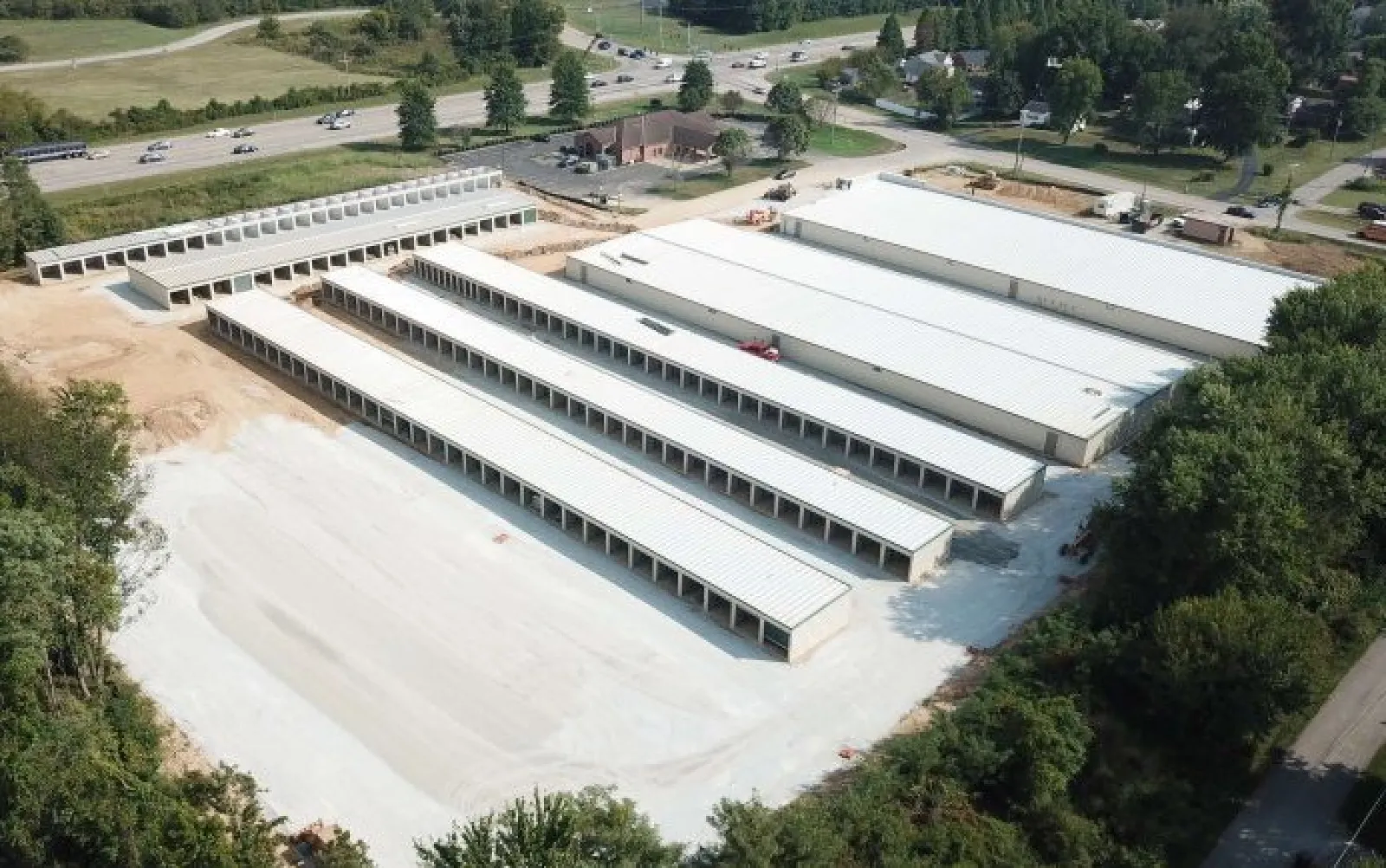 Aerial view of a large storage facility with multiple long white-roofed buildings surrounded by trees and roads.