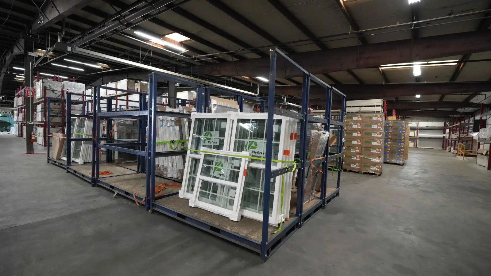 Large warehouse shelving holds packaged windows and building materials under high ceiling lights.