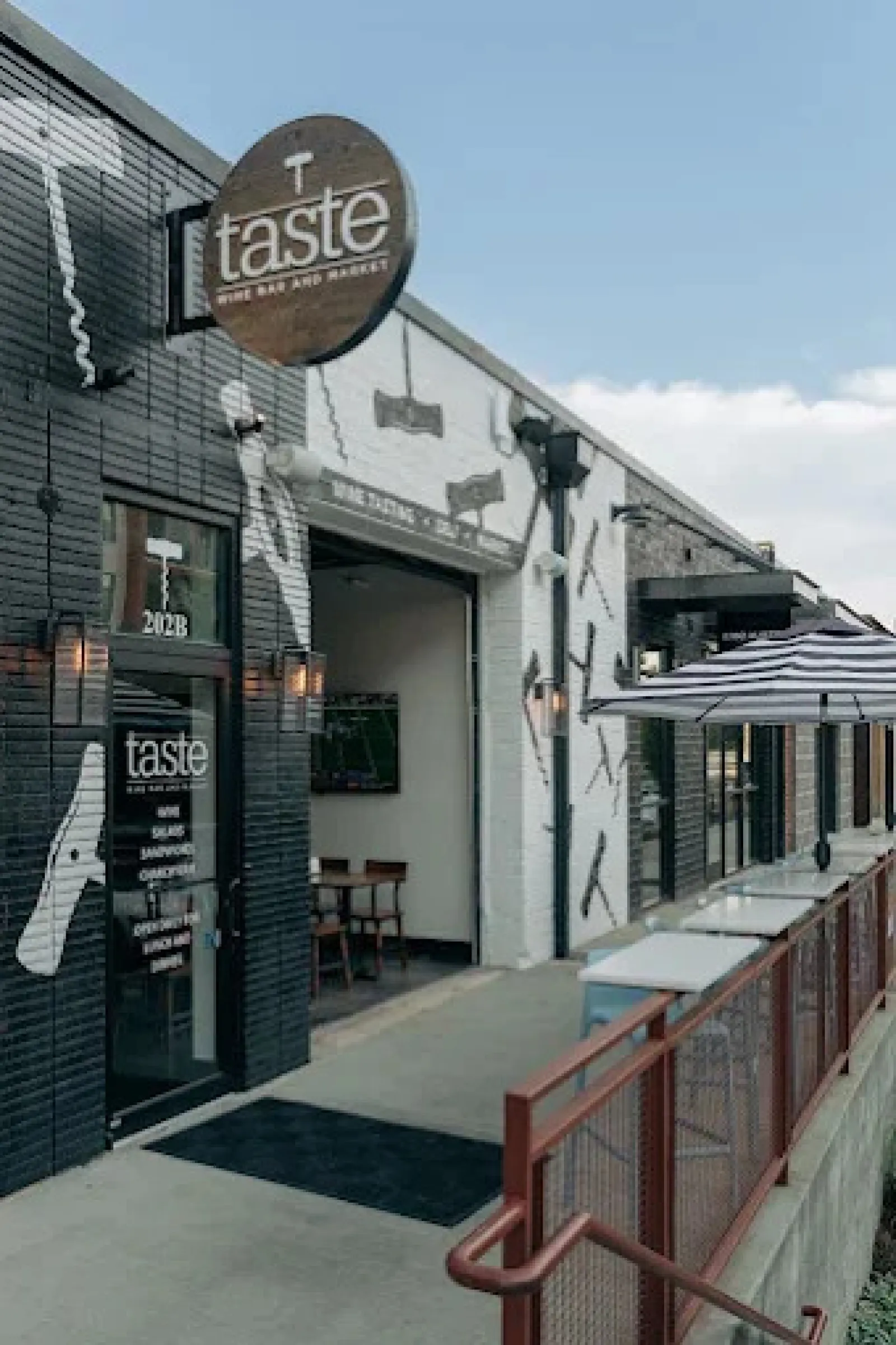 Exterior view of Taste Wine Bar and Market with black and white walls and outdoor seating under umbrella.