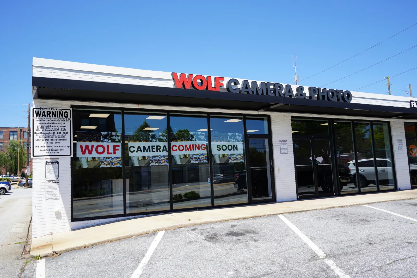 Storefront of Wolf Camera & Photo with signs announcing new store coming soon under clear blue sky.