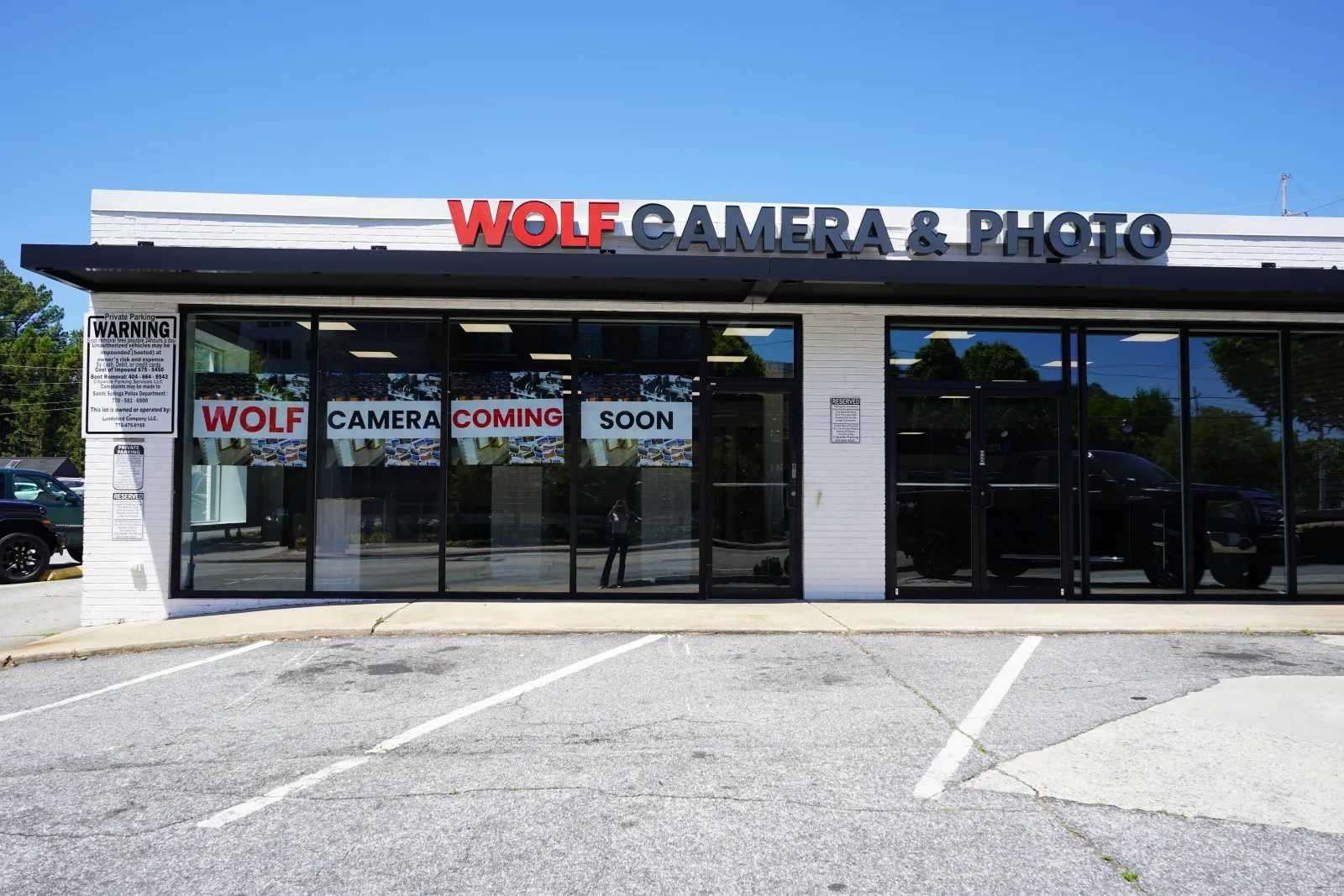 Exterior of Wolf Camera & Photo store with signage announcing opening coming soon on a sunny day.