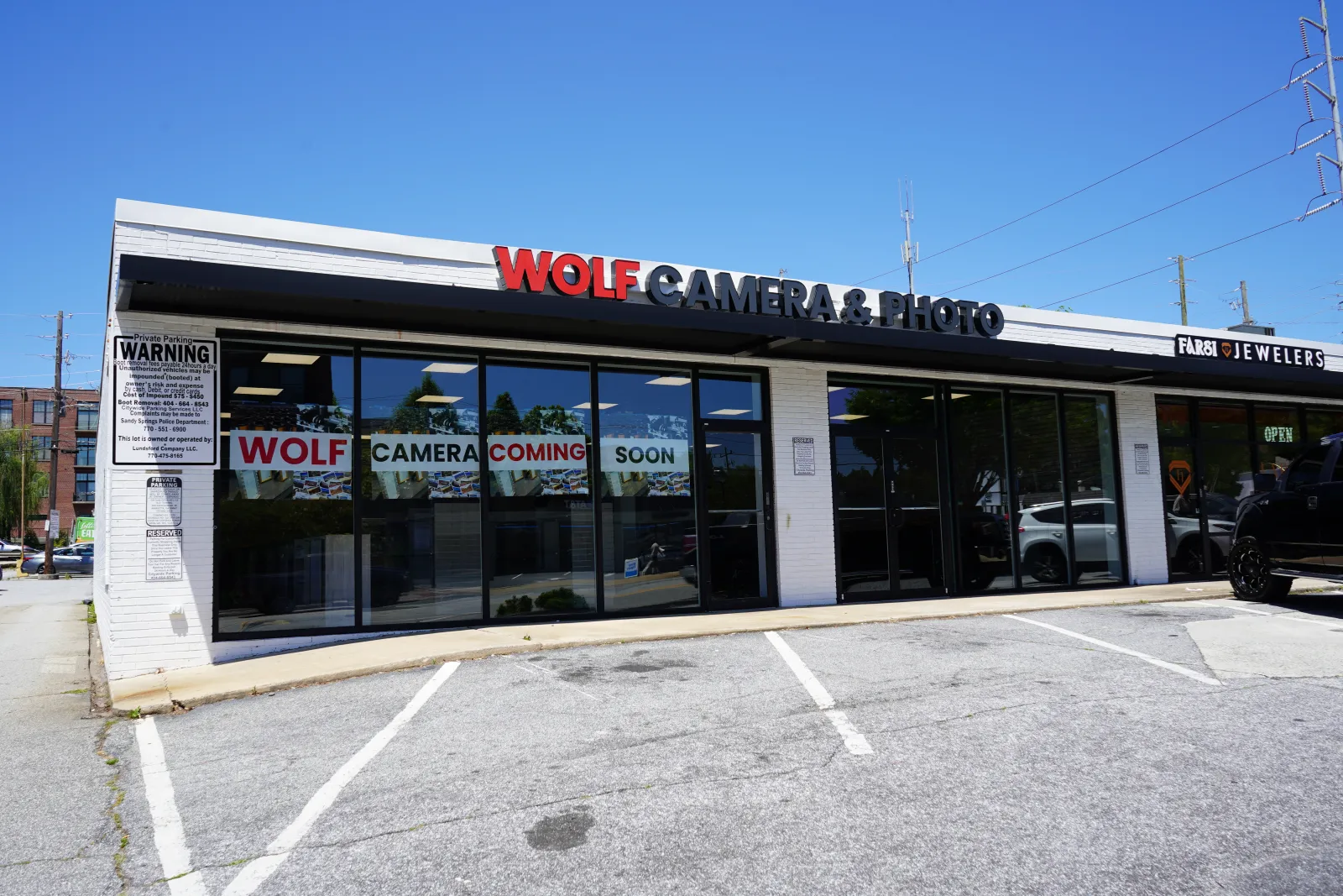 Exterior of Wolf Camera & Photo store with signage and parking lot on a clear sunny day.