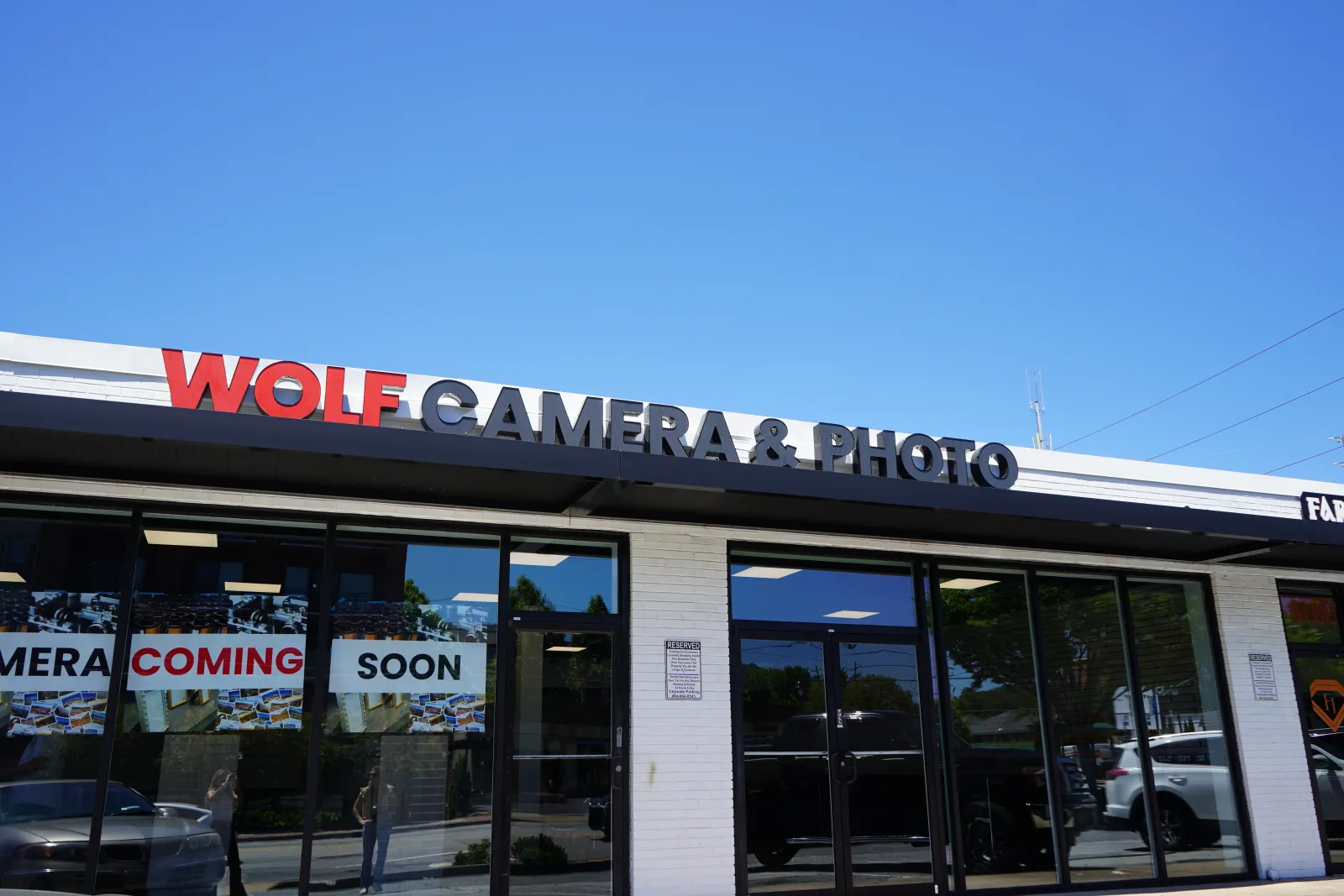 Storefront of Wolf Camera & Photo with signage and Coming Soon banners under a clear blue sky.