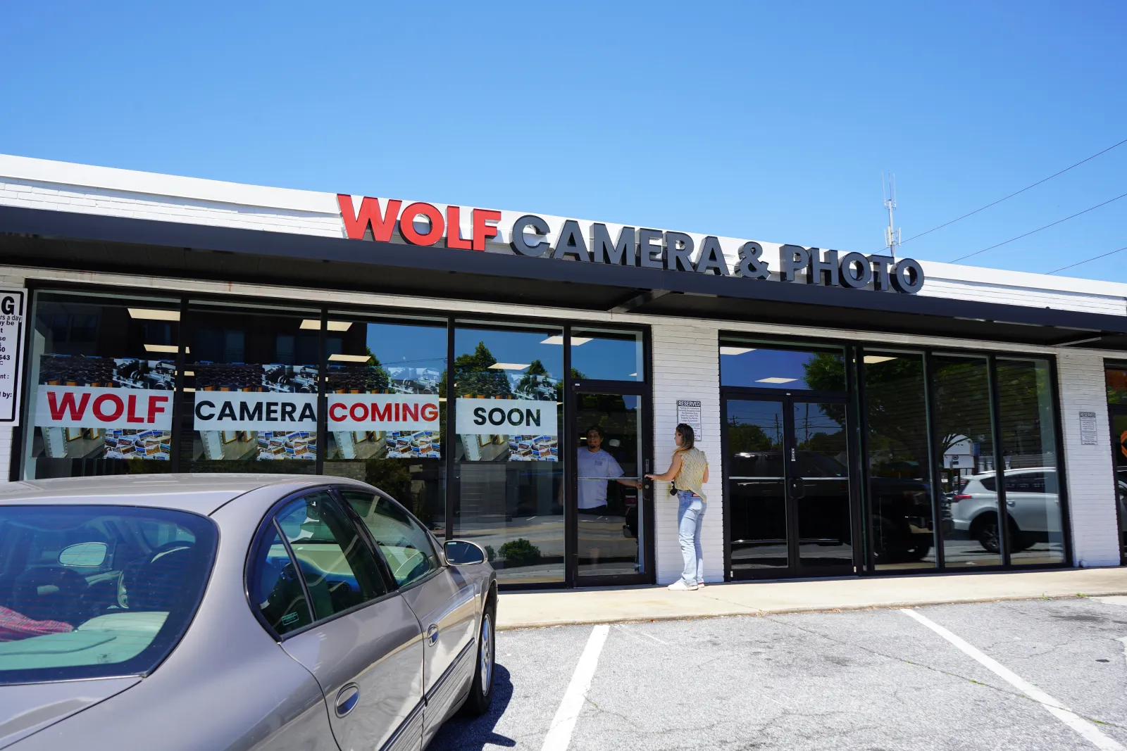 Wolf Camera & Photo store front with signs announcing the camera shop coming soon and people entering the store.