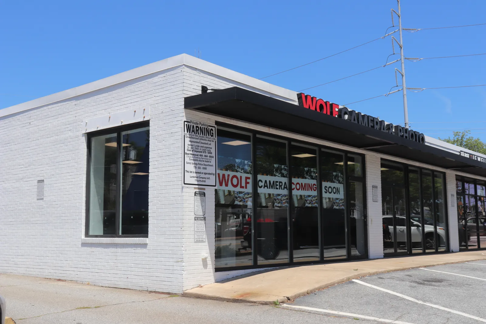 White brick storefront with glass windows displaying Wolf Camera coming soon signs under clear blue sky