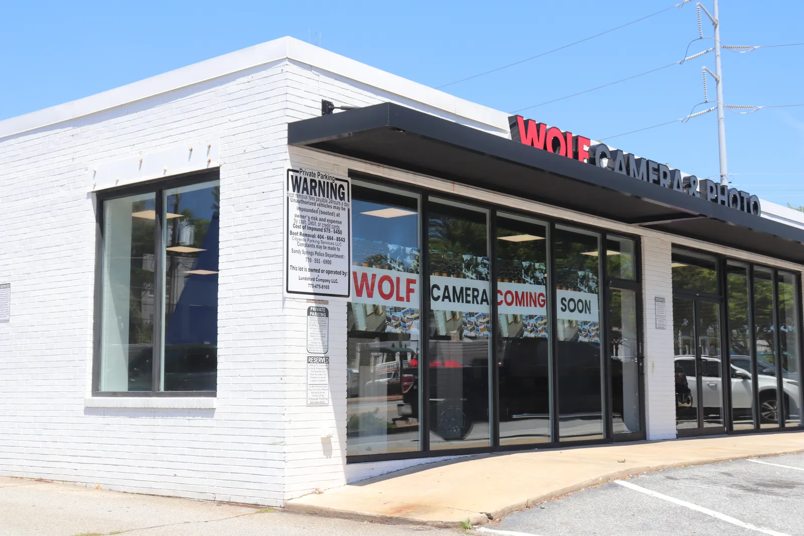 White brick storefront with glass windows displaying Wolf Camera coming soon signage on a sunny day.