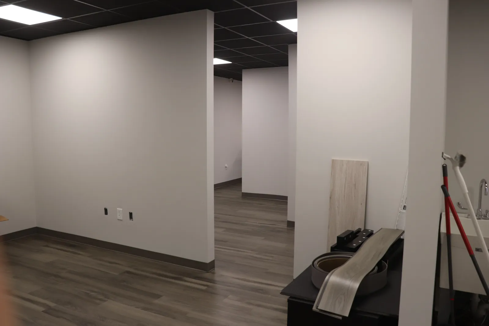 Empty office space with gray walls, wood-look flooring, and various building materials and tools inside.