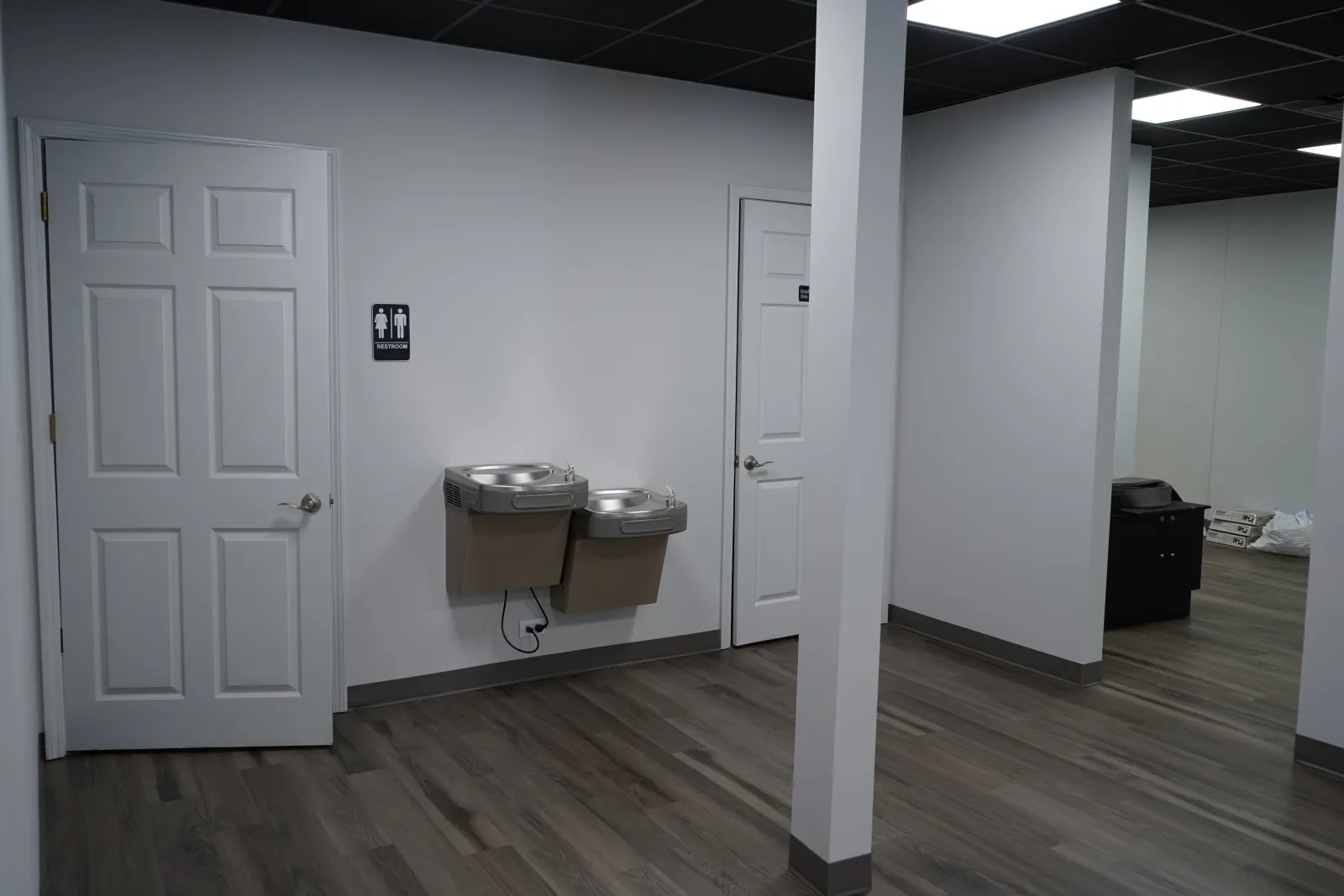 Interior of a modern indoor space with two white doors, dual water fountains, and wood-look flooring.