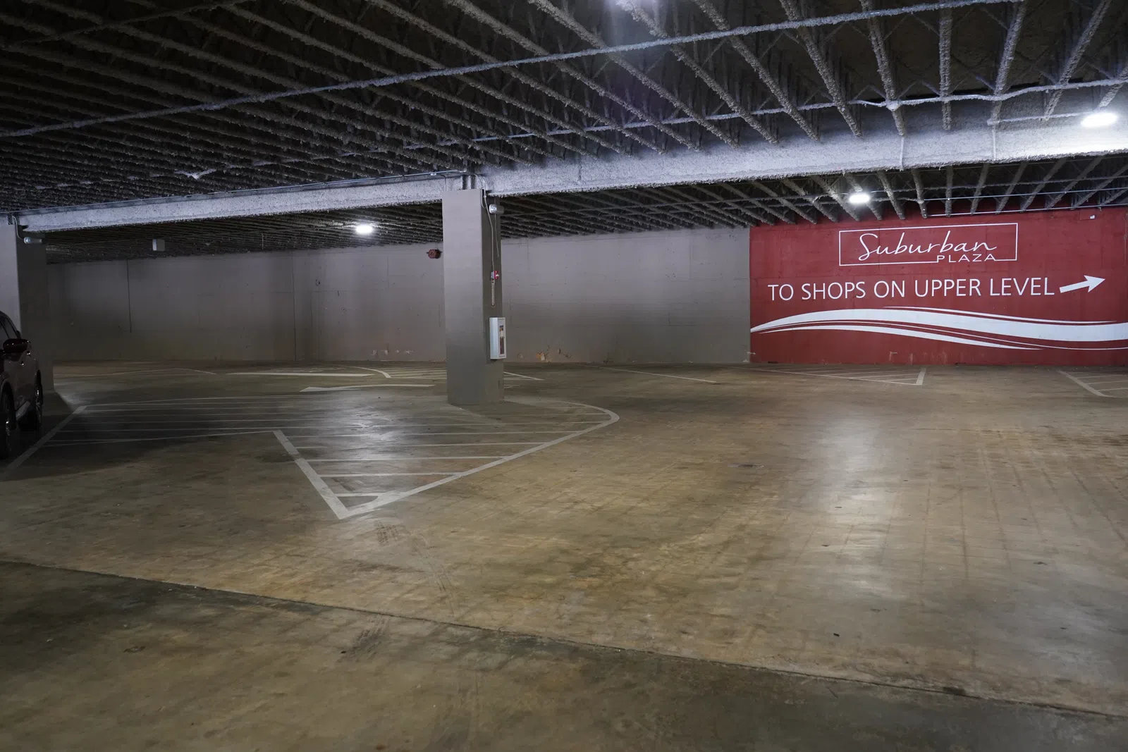 Empty indoor parking garage with concrete floor and a sign directing to shops on the upper level