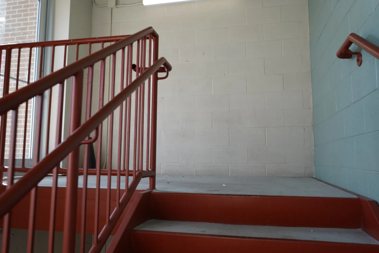 Empty stair landing with red metal handrails and concrete walls painted blue and white in natural light.
