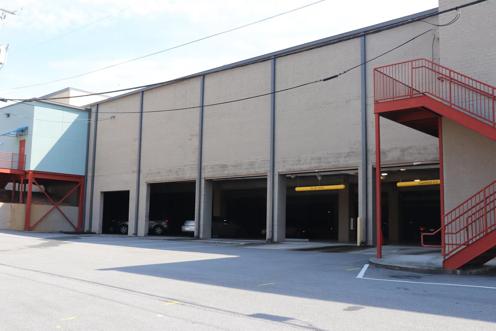 Exterior view of a parking garage with open bays and a red outdoor staircase on the side under a clear sky
