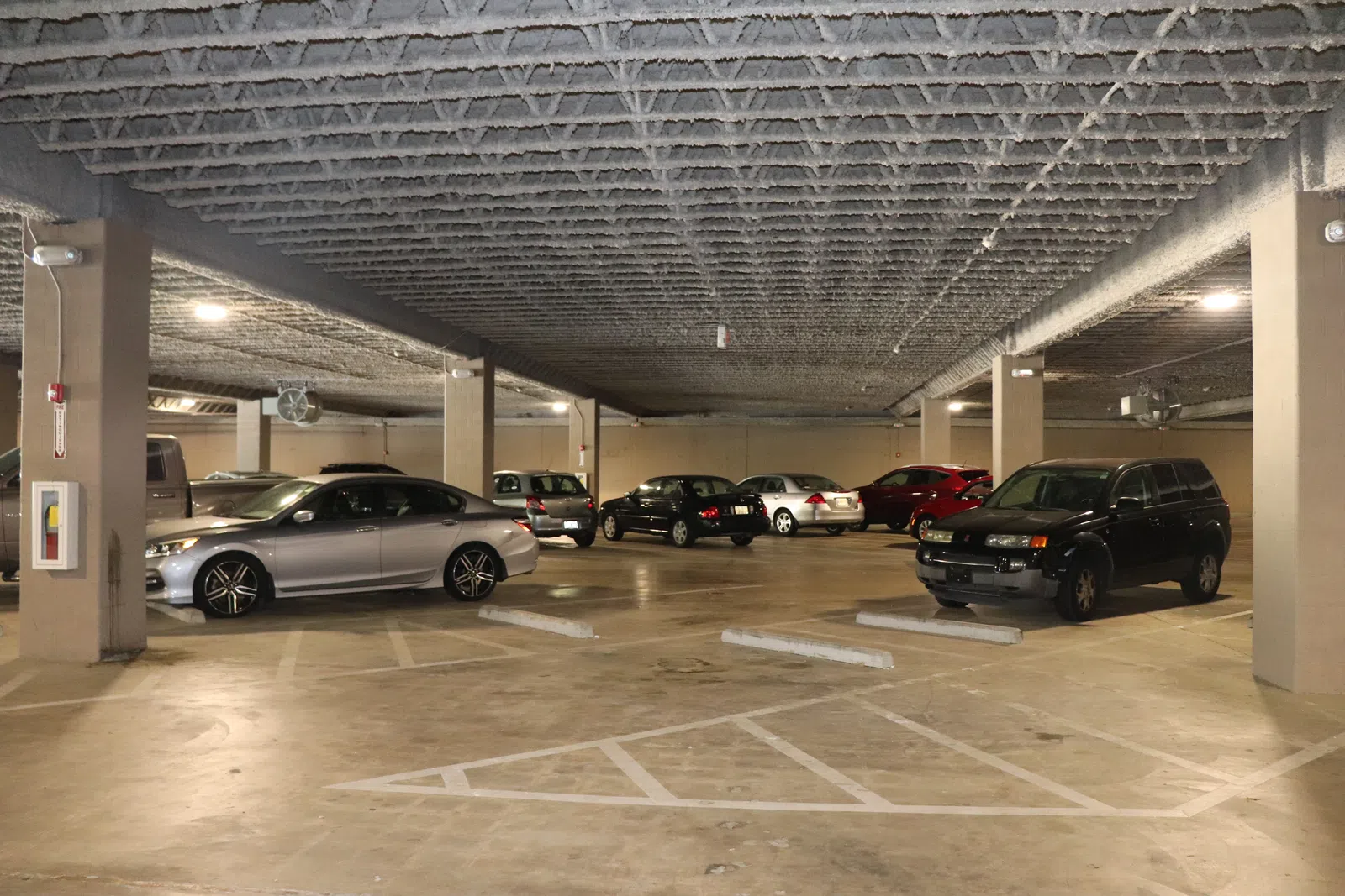 Indoor parking garage with multiple cars parked and concrete pillars supporting the ceiling structure.