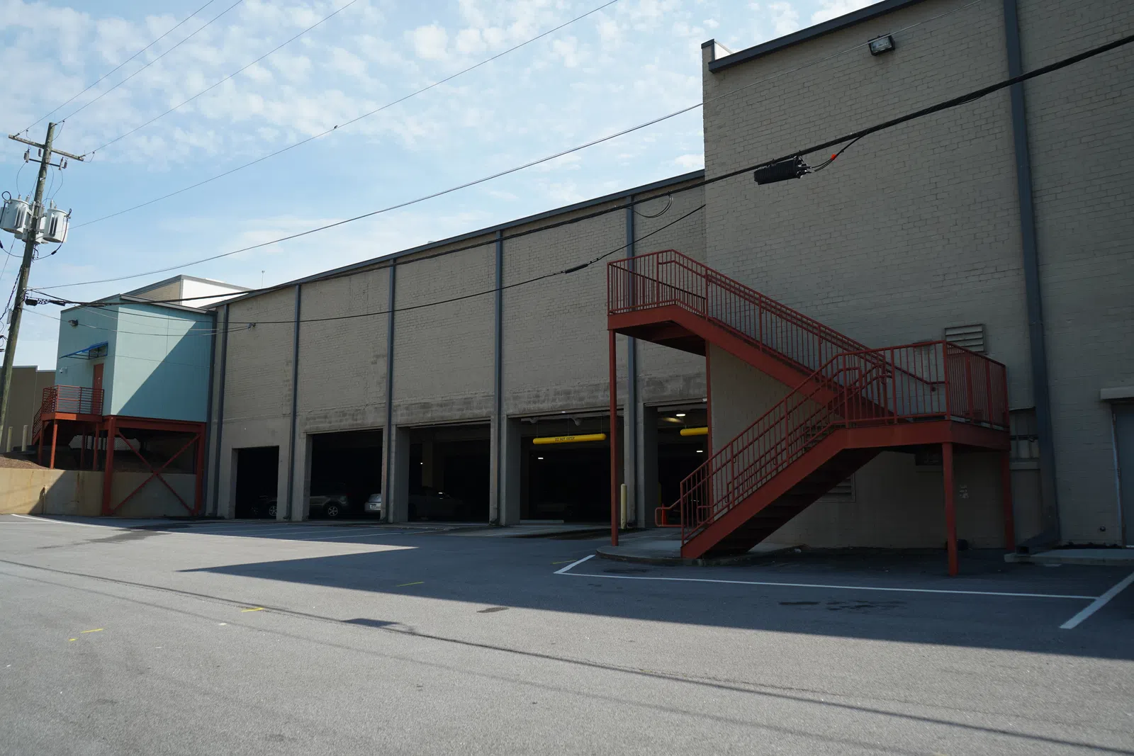 Industrial building with multiple garage doors and red metal staircases under a partly cloudy sky.