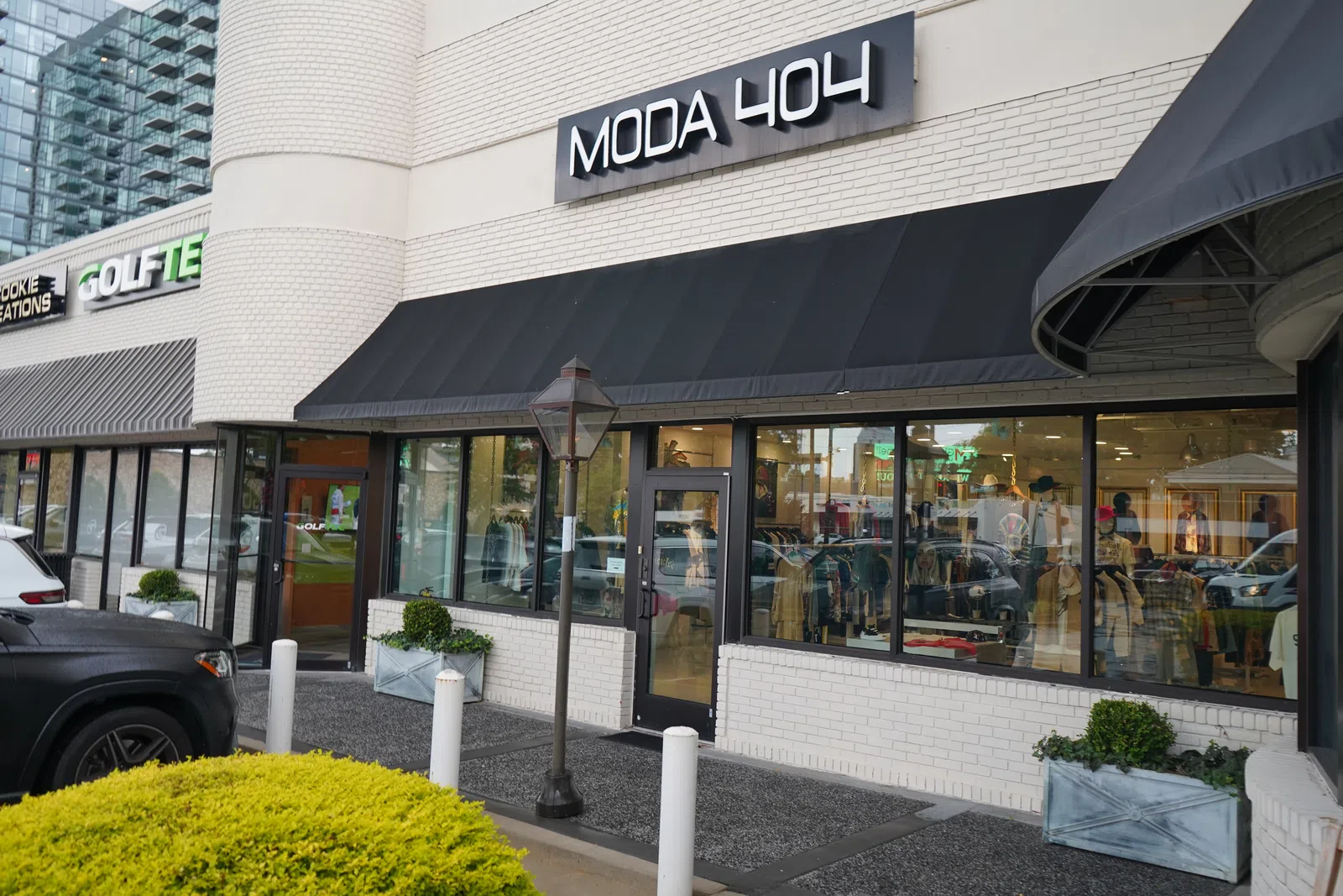 Moda 404 storefront with black awning on white brick building, adjacent to Golftes and Cookie Creations shops.