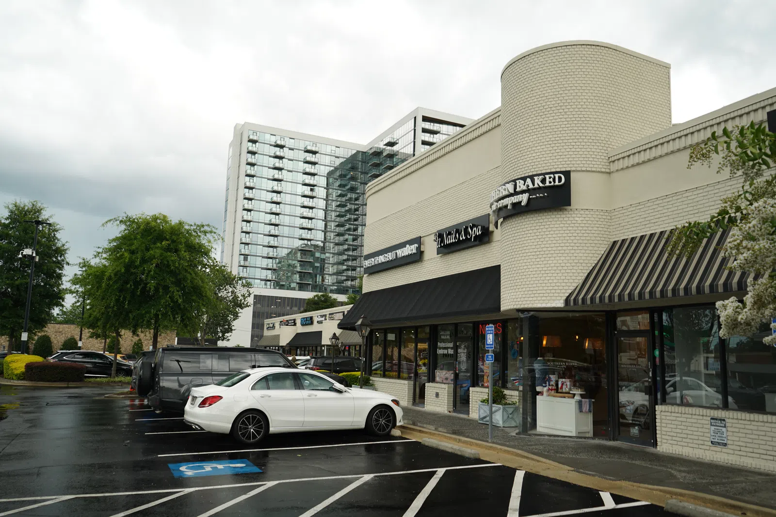 White car parked outside a brick strip mall with businesses including a nail and spa salon on a cloudy day