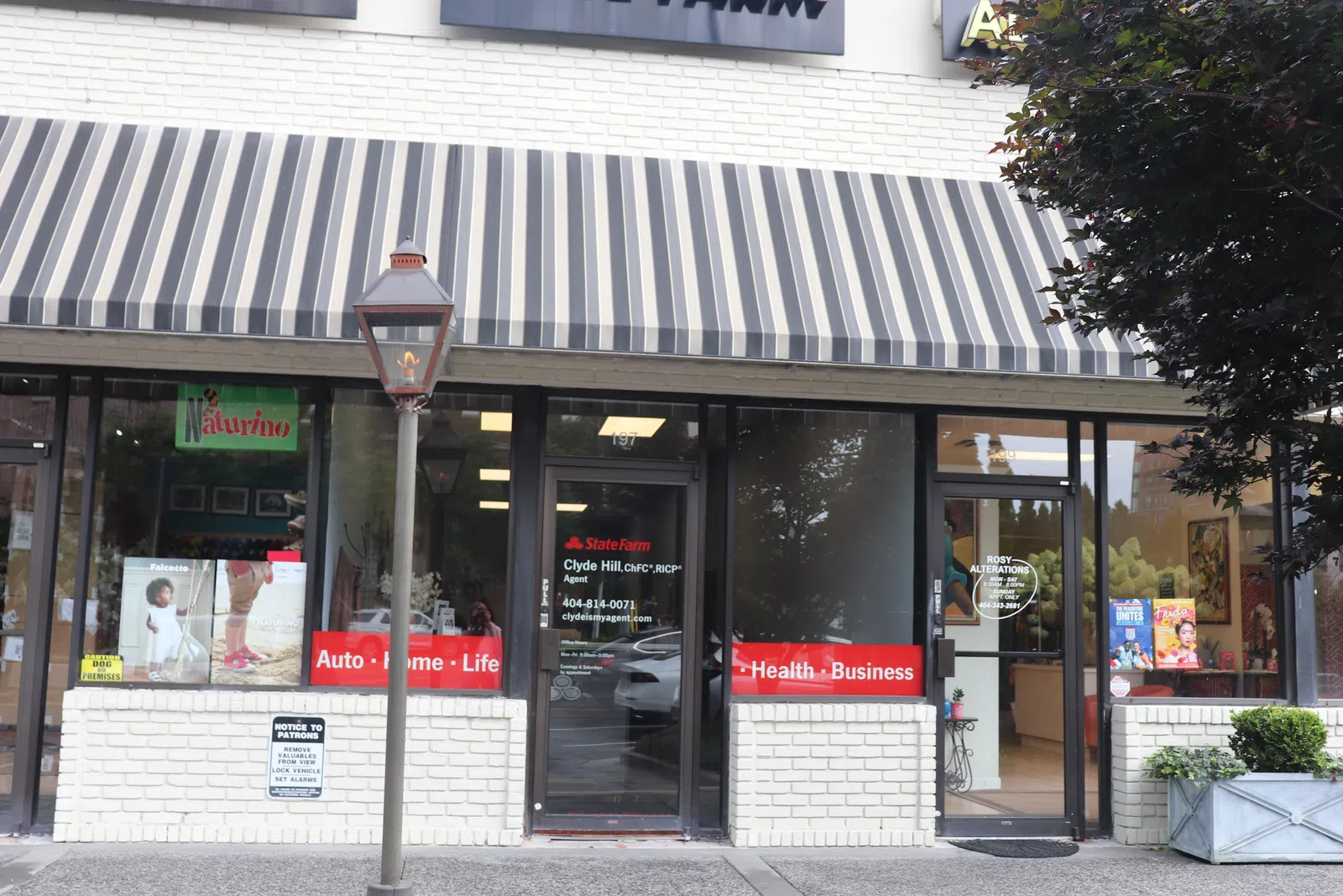 State Farm insurance office storefront with striped awning, red signage, and brick exterior on sunny day