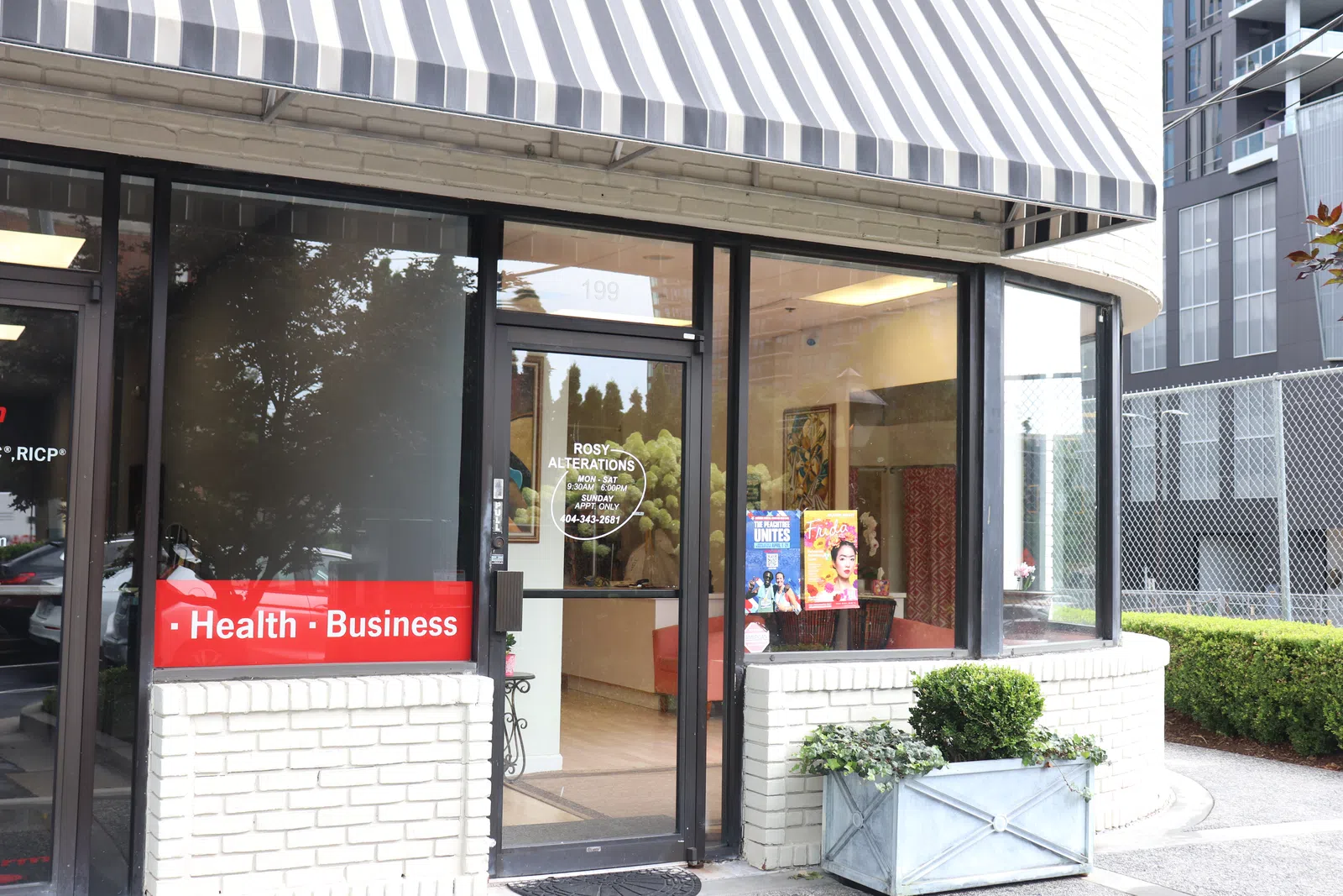 Street view of Rosy Alterations shop with striped awning, glass door, and window displays in urban setting.