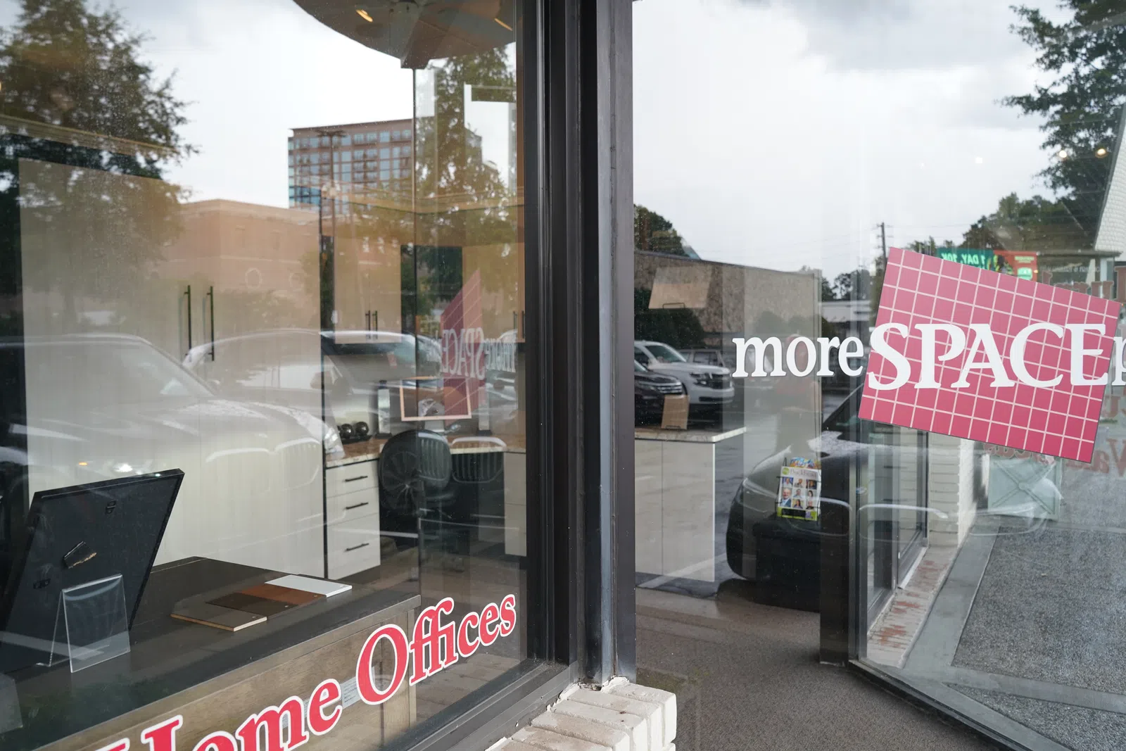 Storefront glass windows displaying signage for office space rental with reflections of cars and nearby buildings.