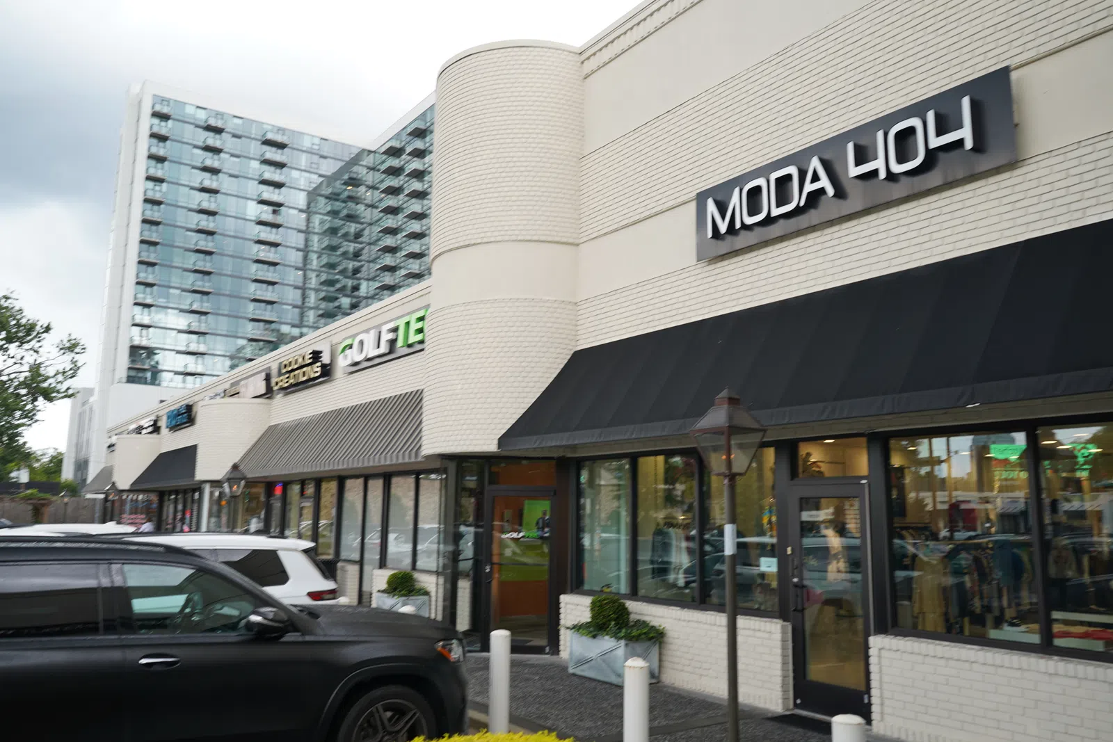 Street view of modern retail shops with Moda 404 and other store signs under a cloudy sky.