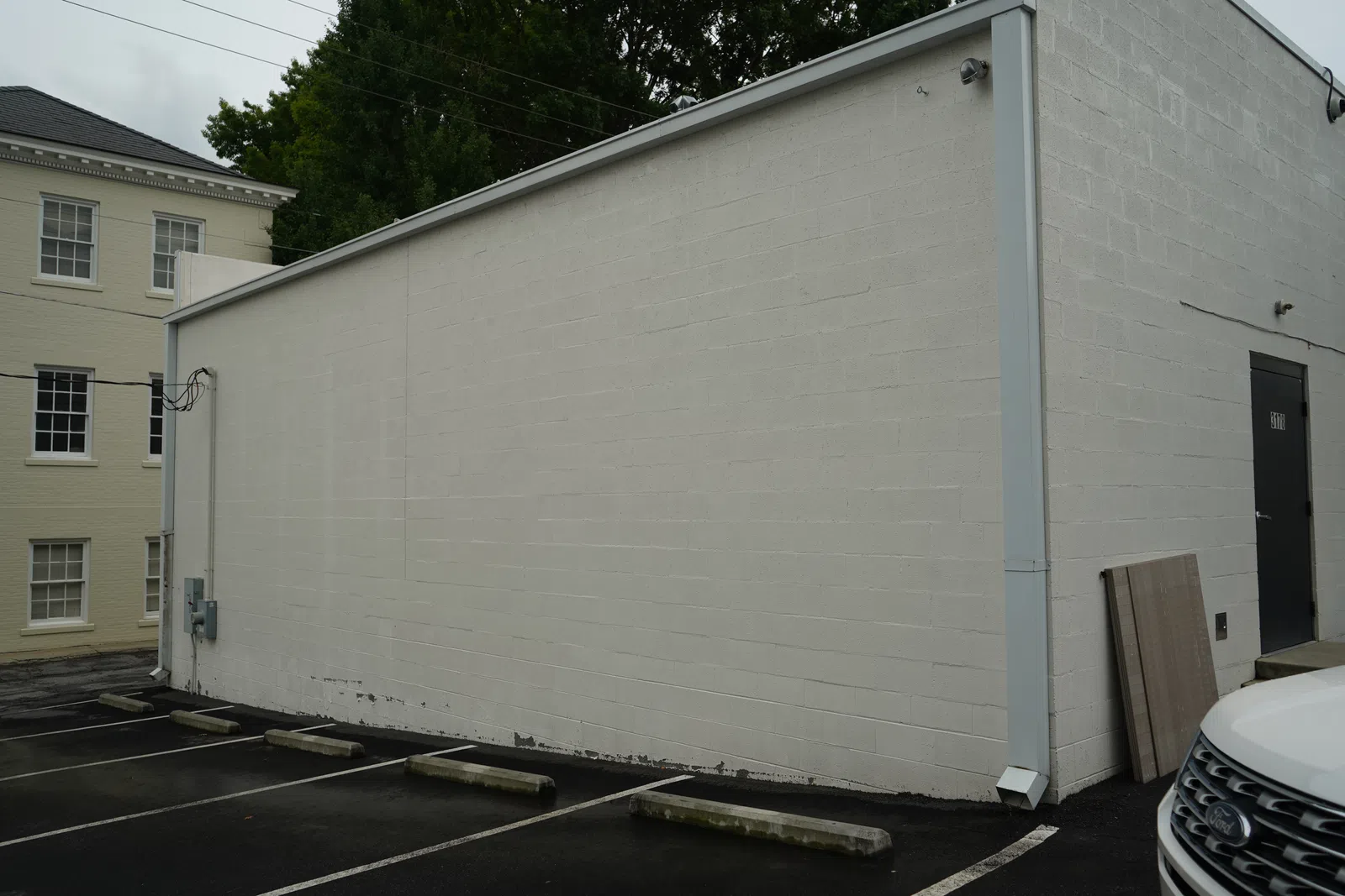 Empty parking spaces beside a plain white brick building with a black door on an overcast day.