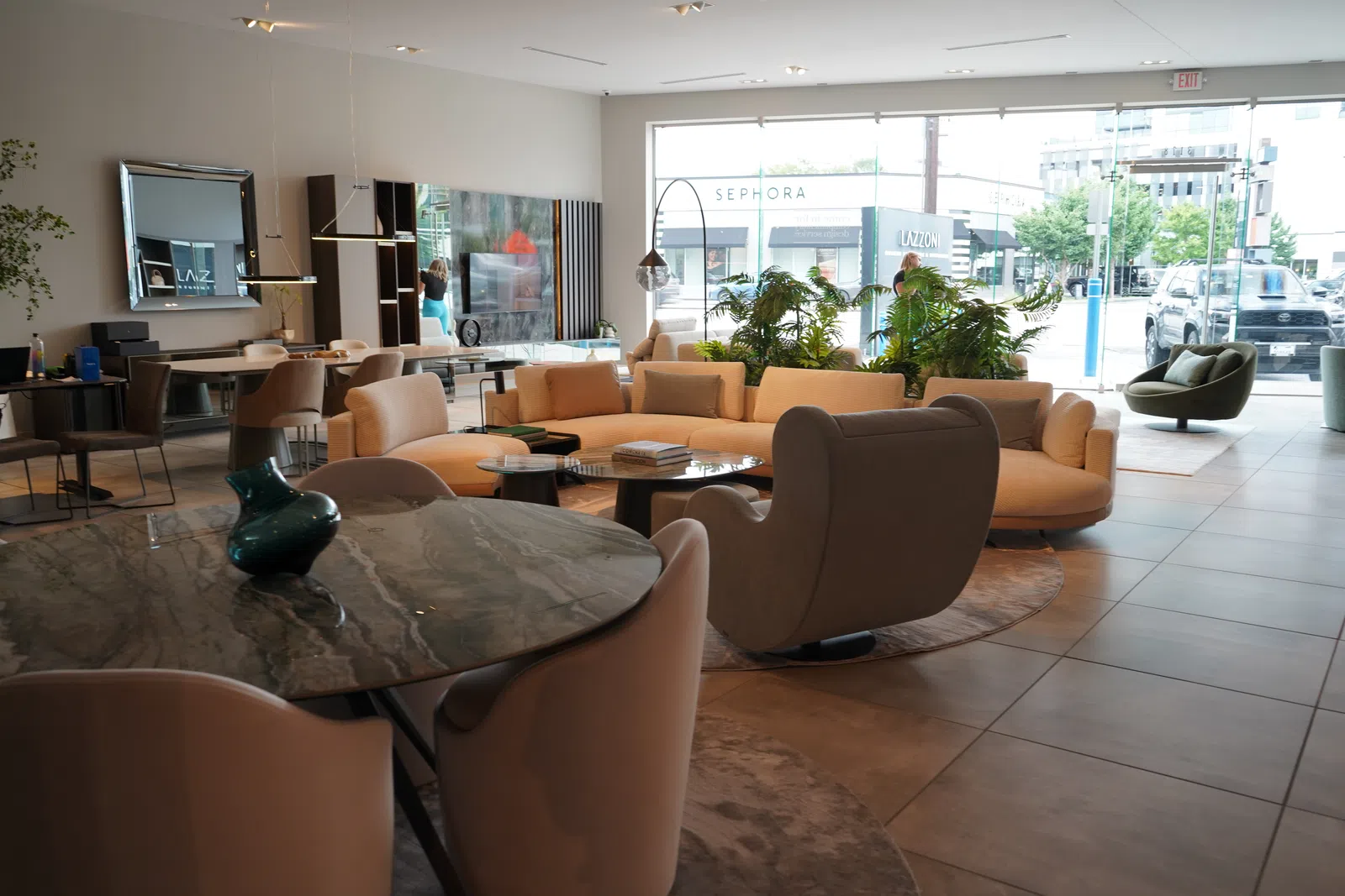 Modern living room with beige sectional sofa, armchairs, marble-top table, and large windows with natural light.