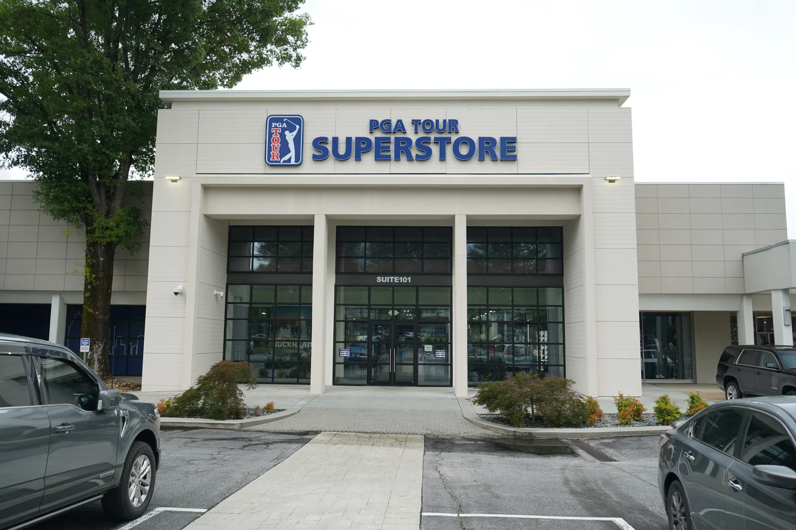 Exterior view of the PGA Tour Superstore building with parked cars and trees in front under overcast sky