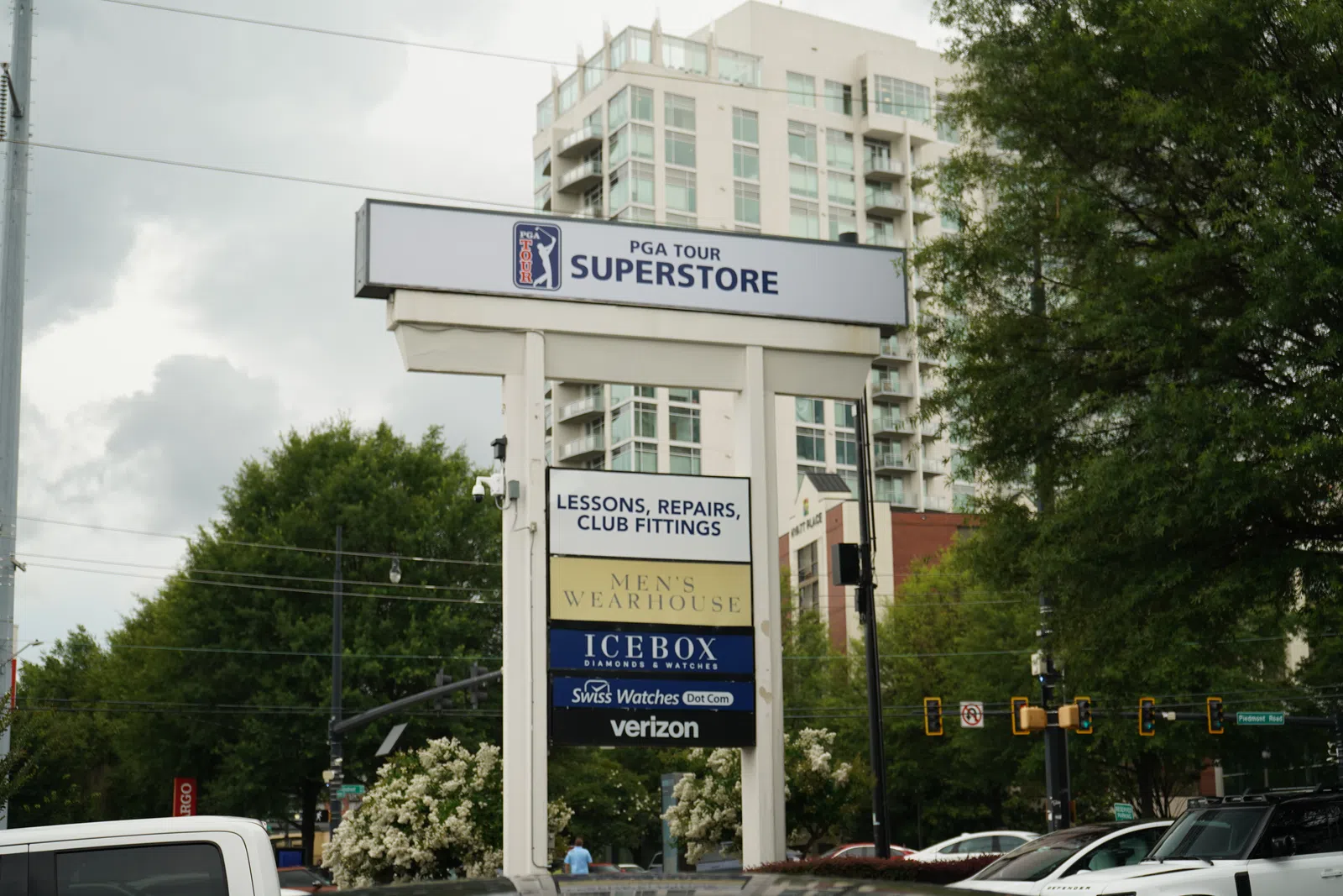 Outdoor signpost displaying PGA Tour Superstore and various retail business logos with cityscape background.