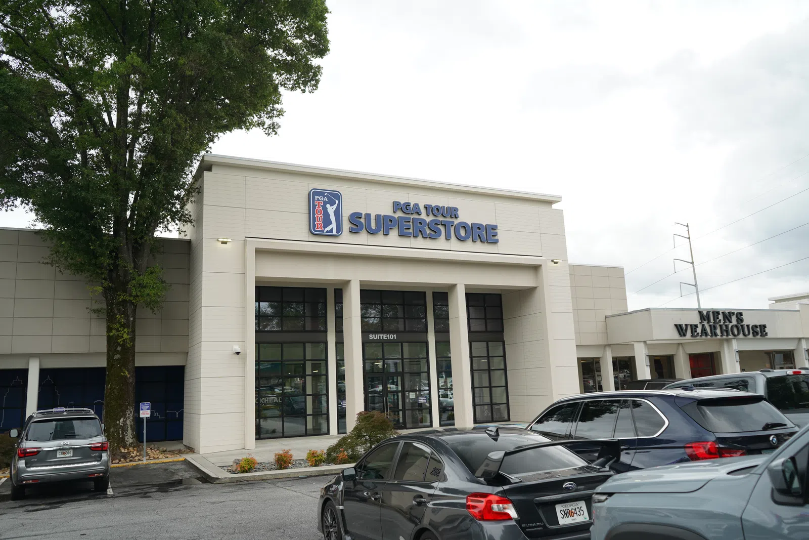Exterior view of PGA Tour Superstore with parked cars and Men's Wearhouse store beside it on cloudy day