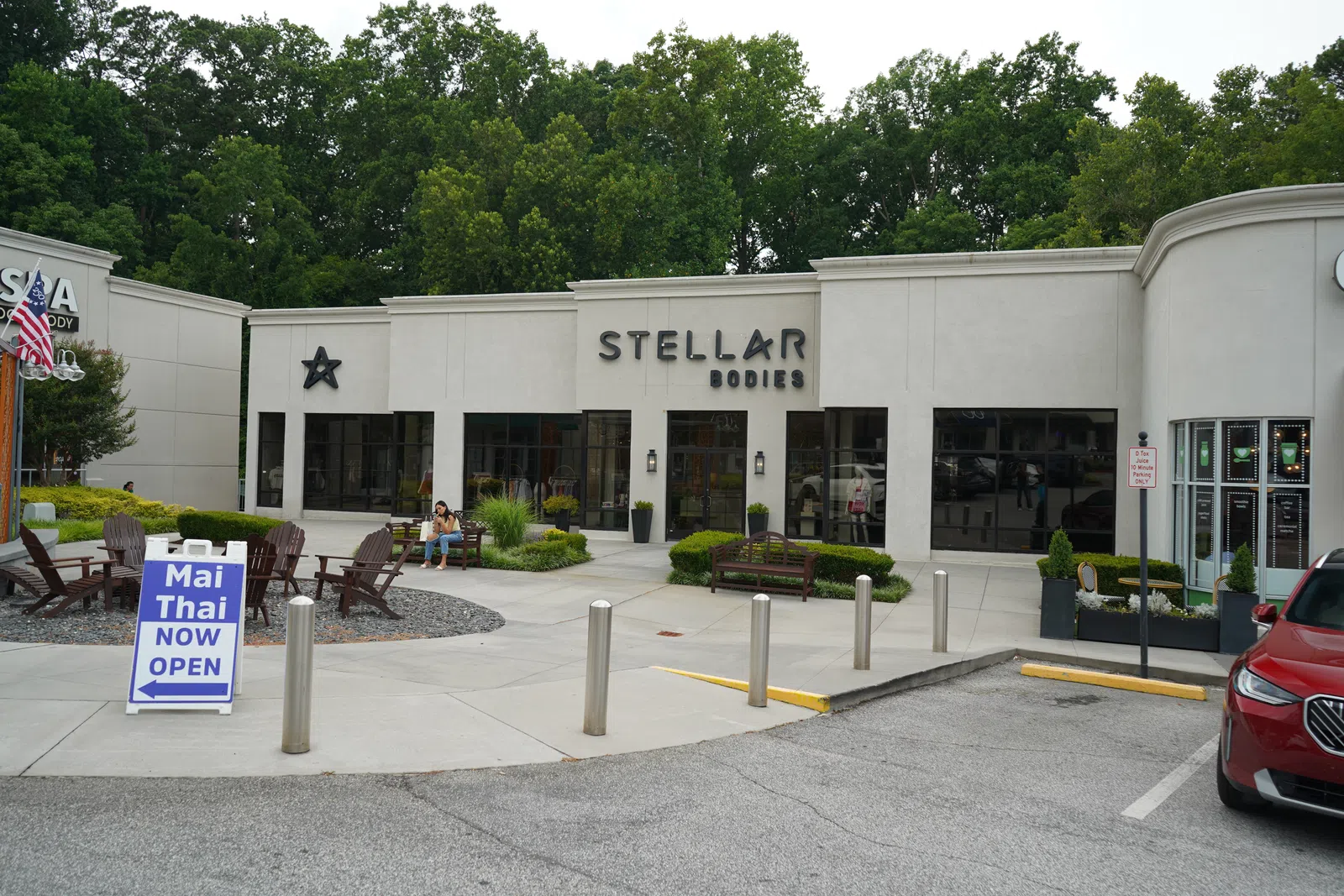 Exterior view of Stellar Bodies storefront with outdoor seating and Mai Thai restaurant open sign in front.