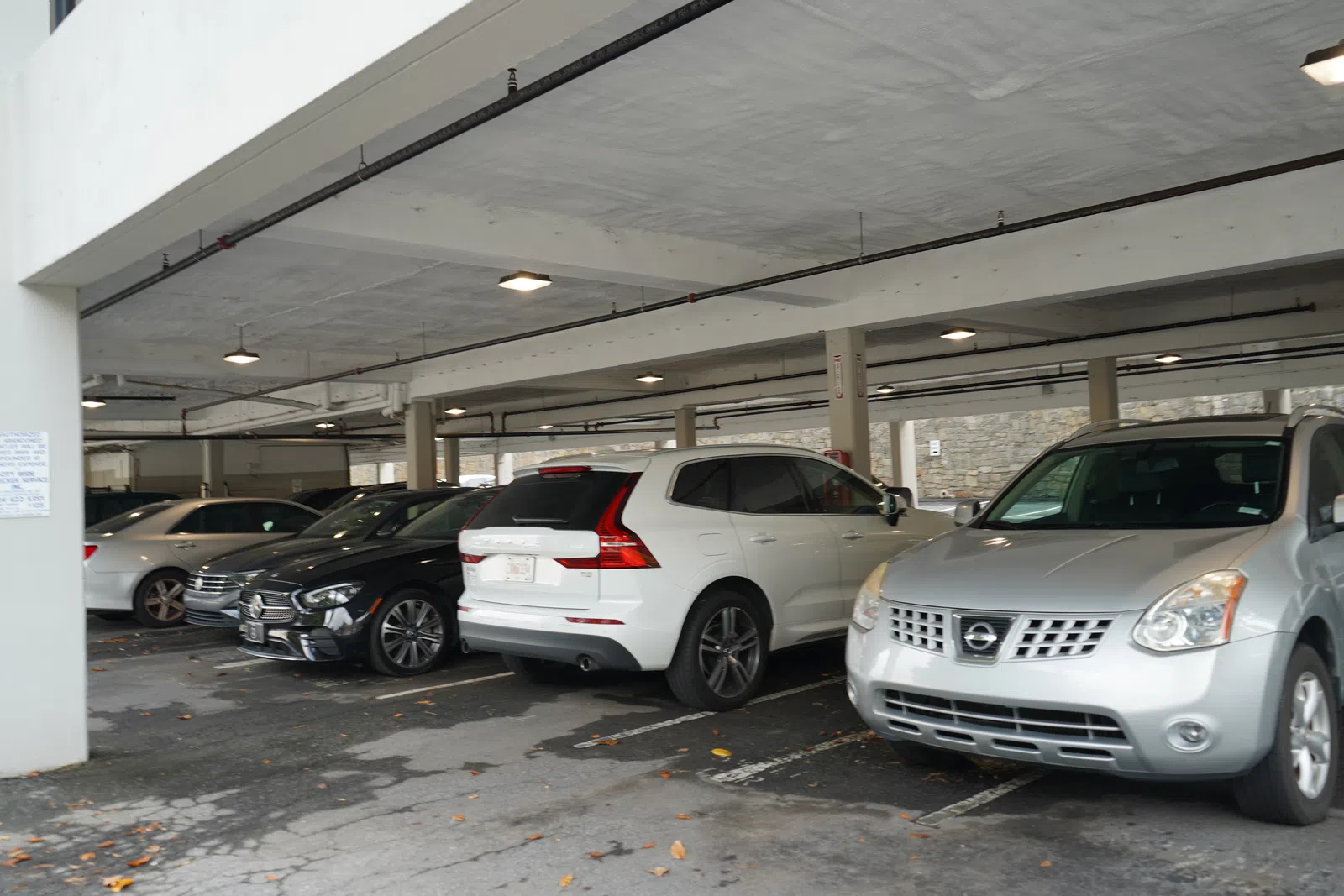 Cars parked in an indoor parking garage with concrete ceiling and pillars, showing various car models and colors.