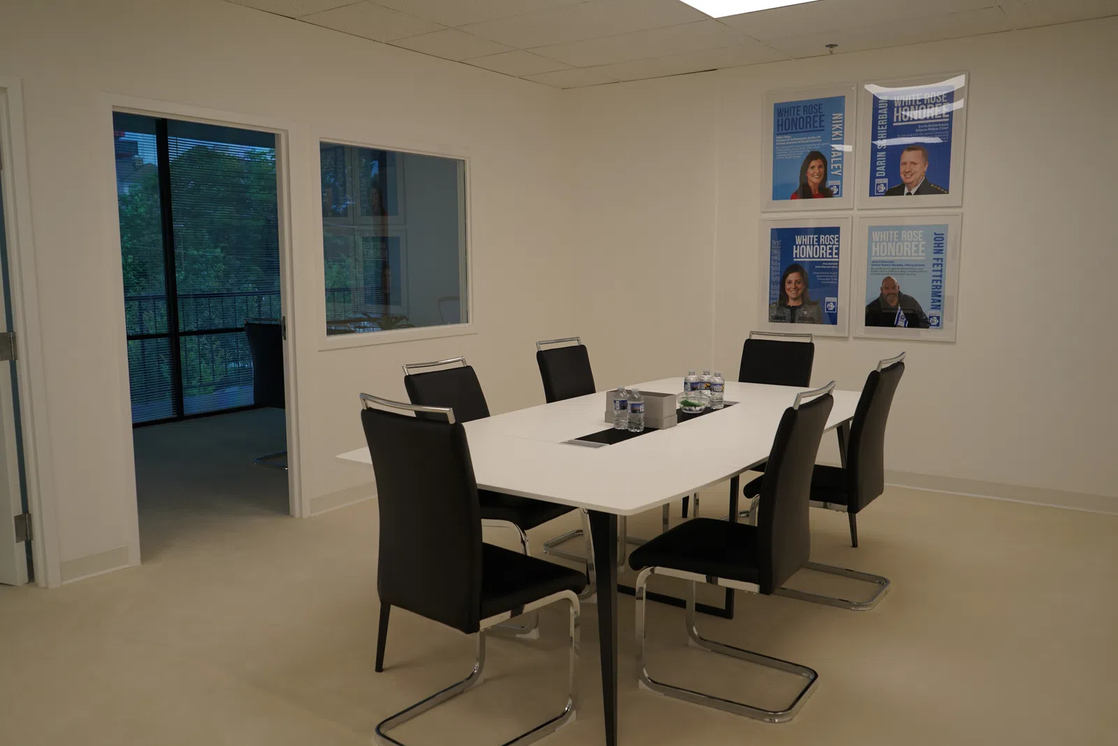 Modern conference room with white table, six black chairs, water bottles, and framed accolades on wall.