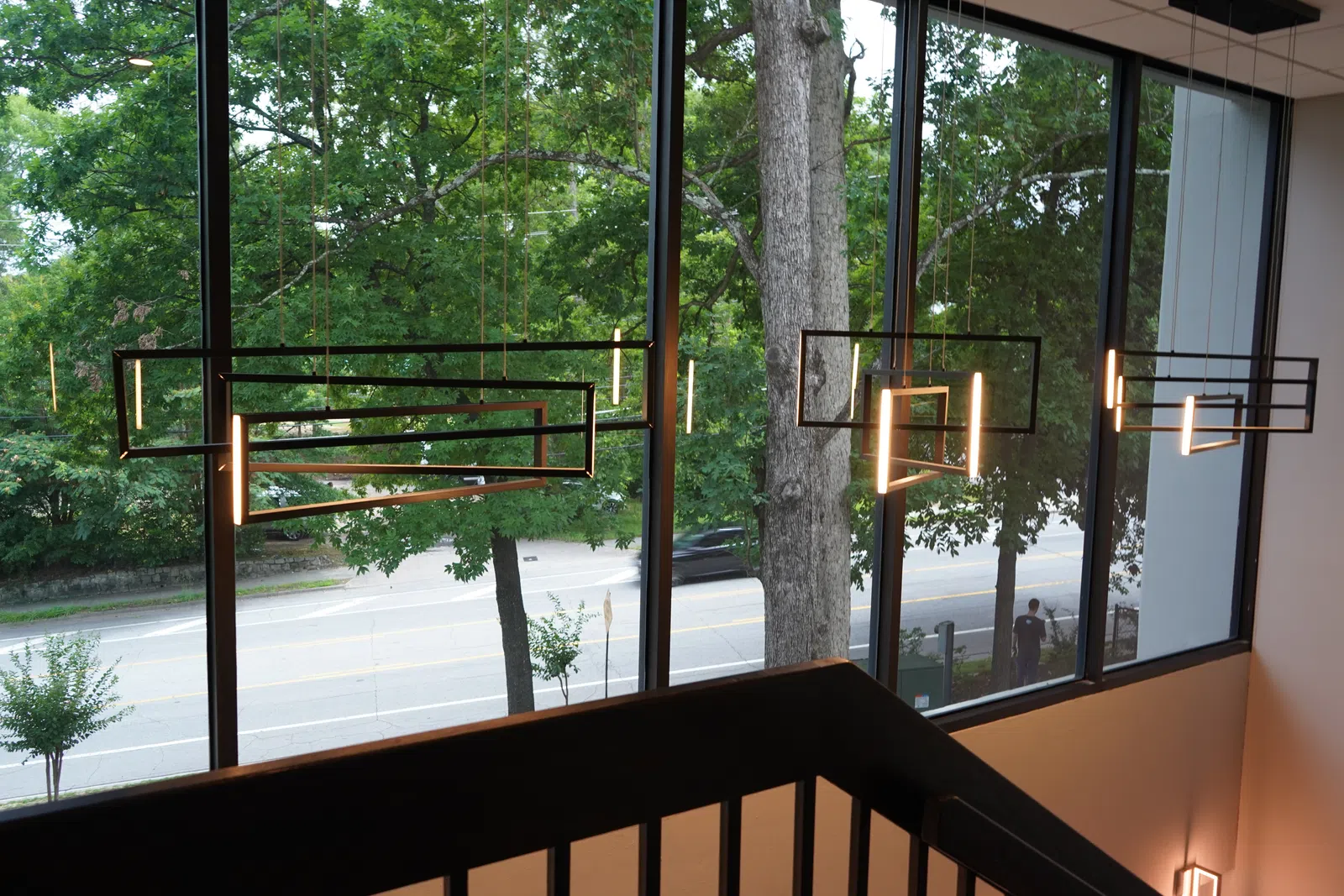 Modern geometric pendant lights hanging in front of large windows overlooking a tree-lined street.