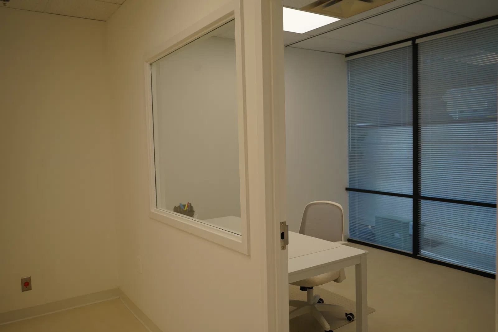 Minimalist office space with a white desk, office chair, and large window with blinds.