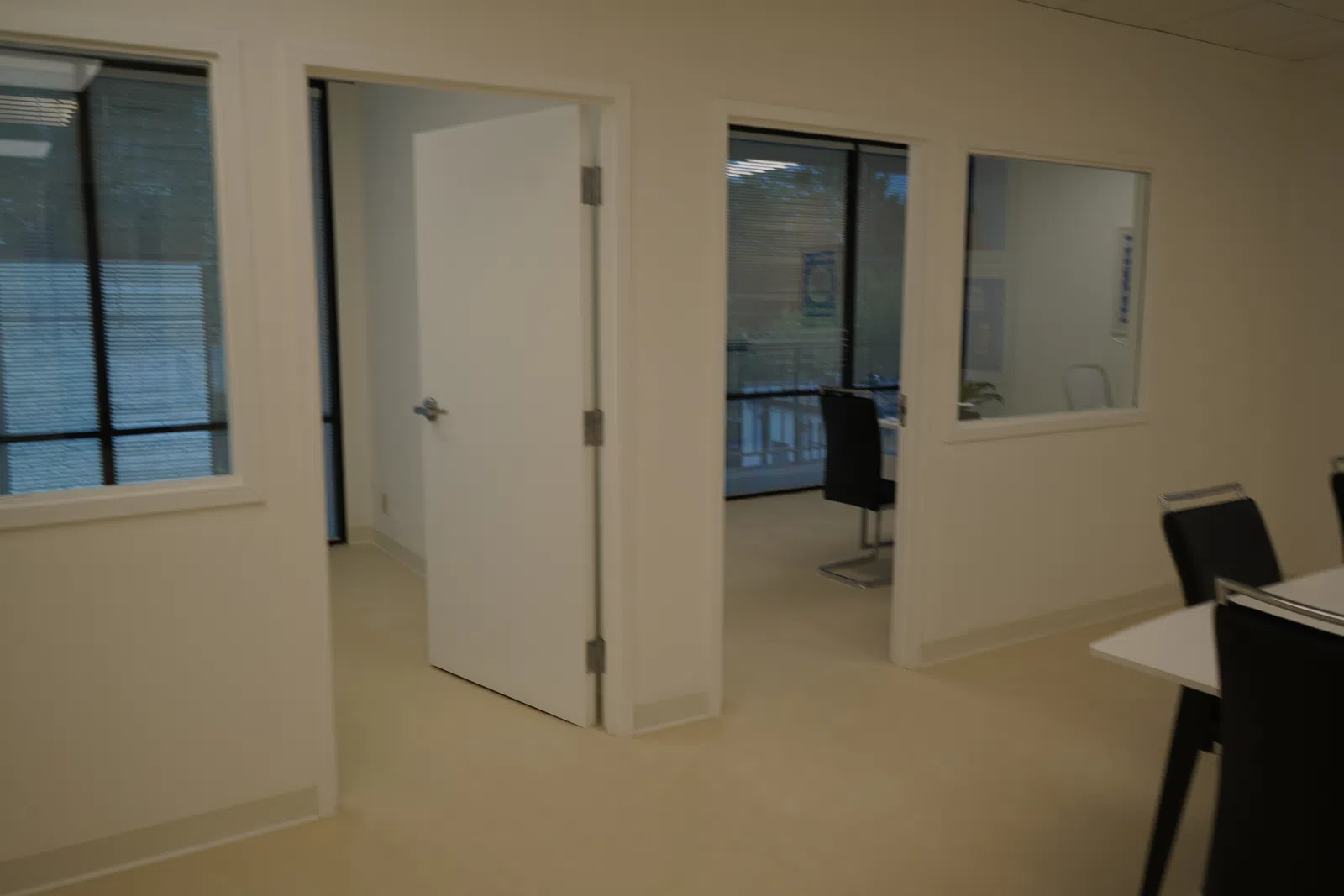 Interior office space with open white doors, glass windows, black chairs, and beige flooring in a modern setting