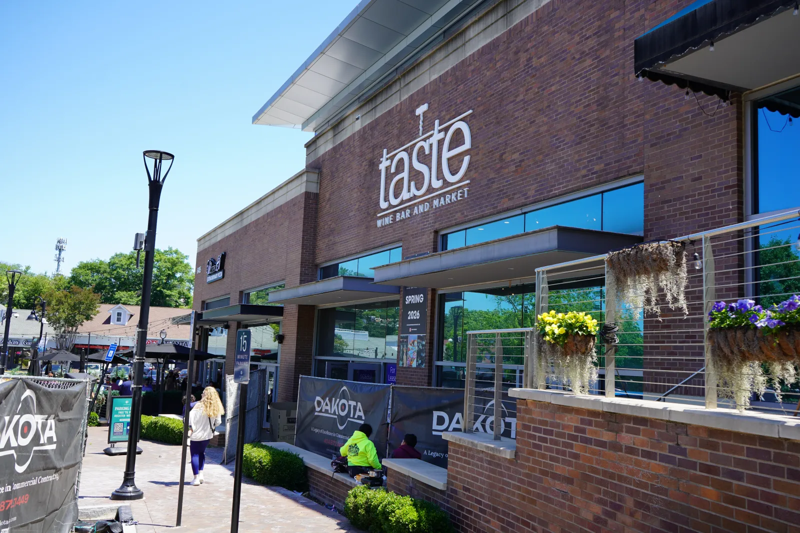 Taste Wine Bar and Market exterior with outdoor seating, brick facade, and flower planters under clear blue sky.