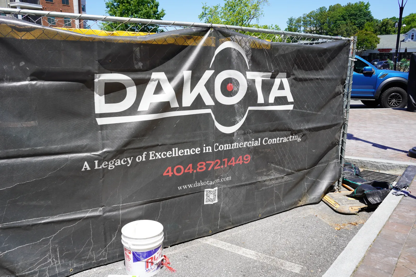 Black fence banner with Dakota logo and contact info for commercial contracting at a construction site.