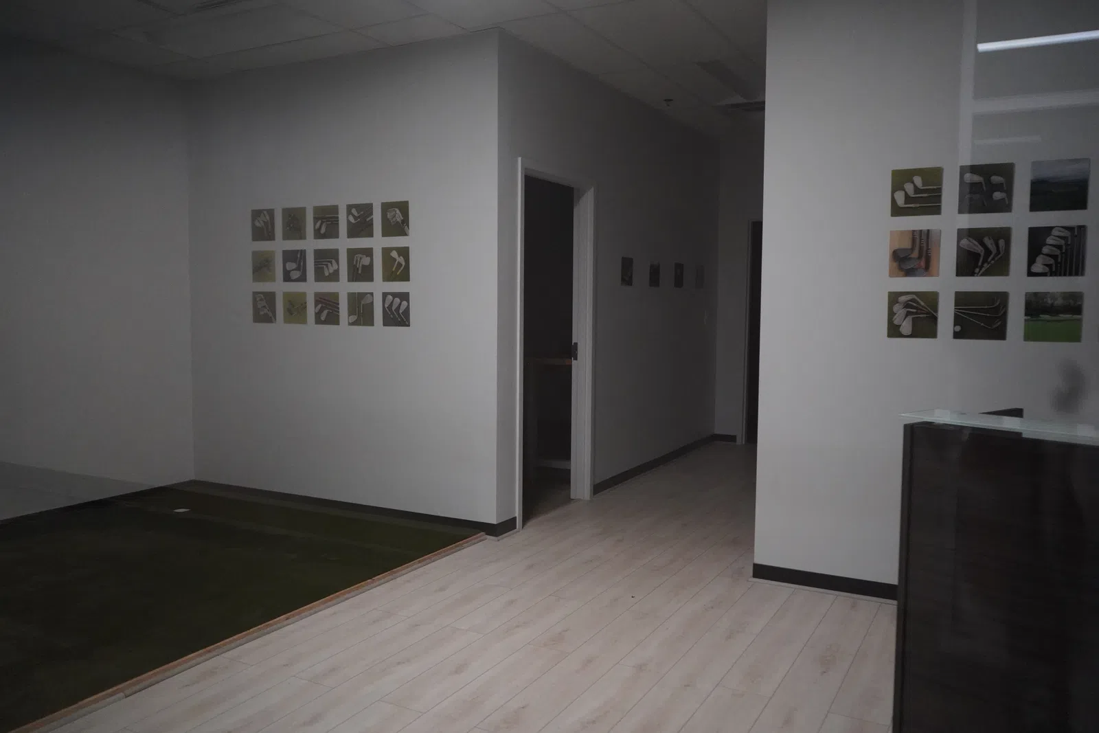 Modern indoor golf practice area with artificial turf, light wood flooring, and visual guides on white walls.