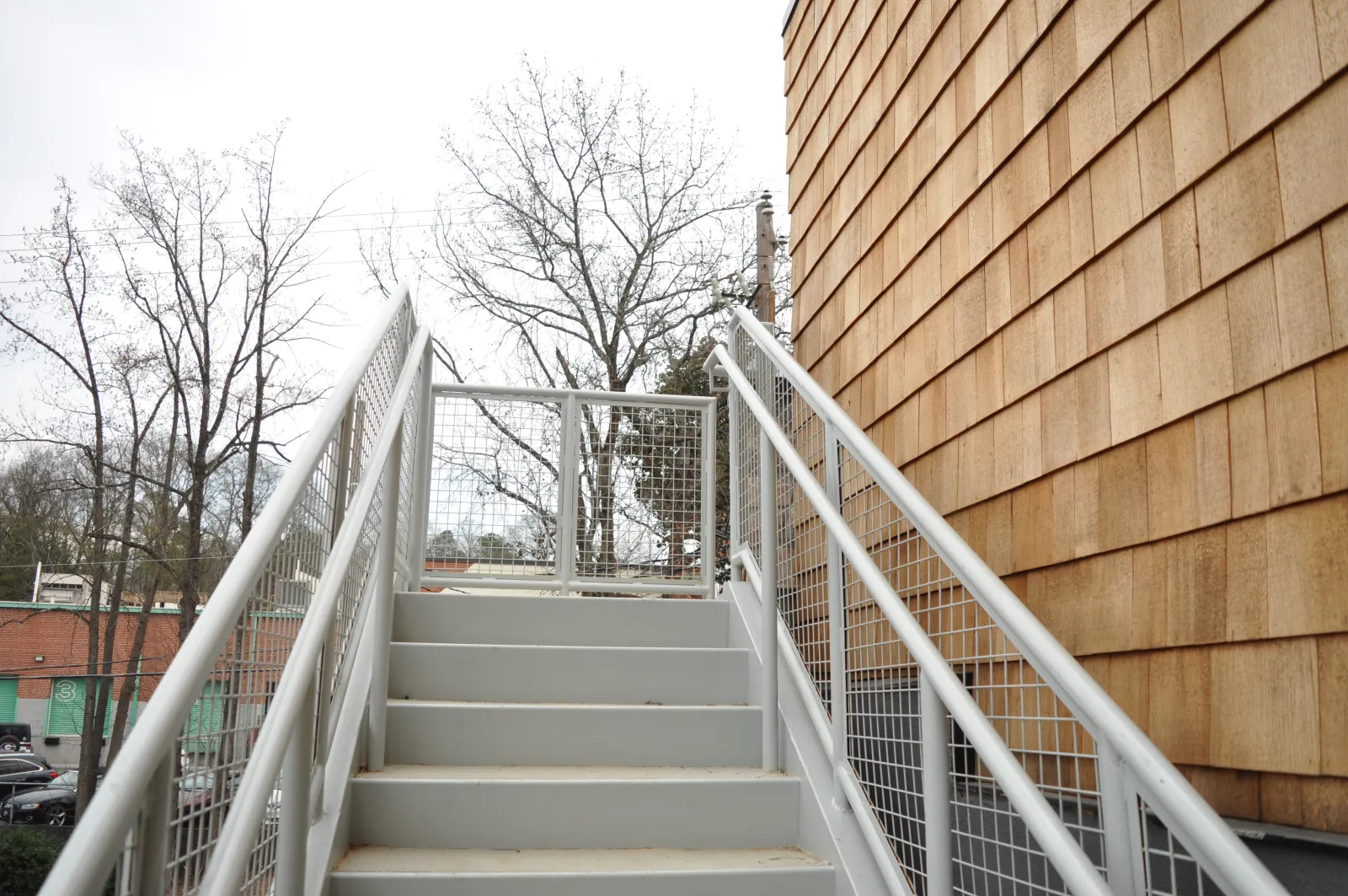 Metal outdoor staircase with safety railings next to a wooden shingle sided building on cloudy day