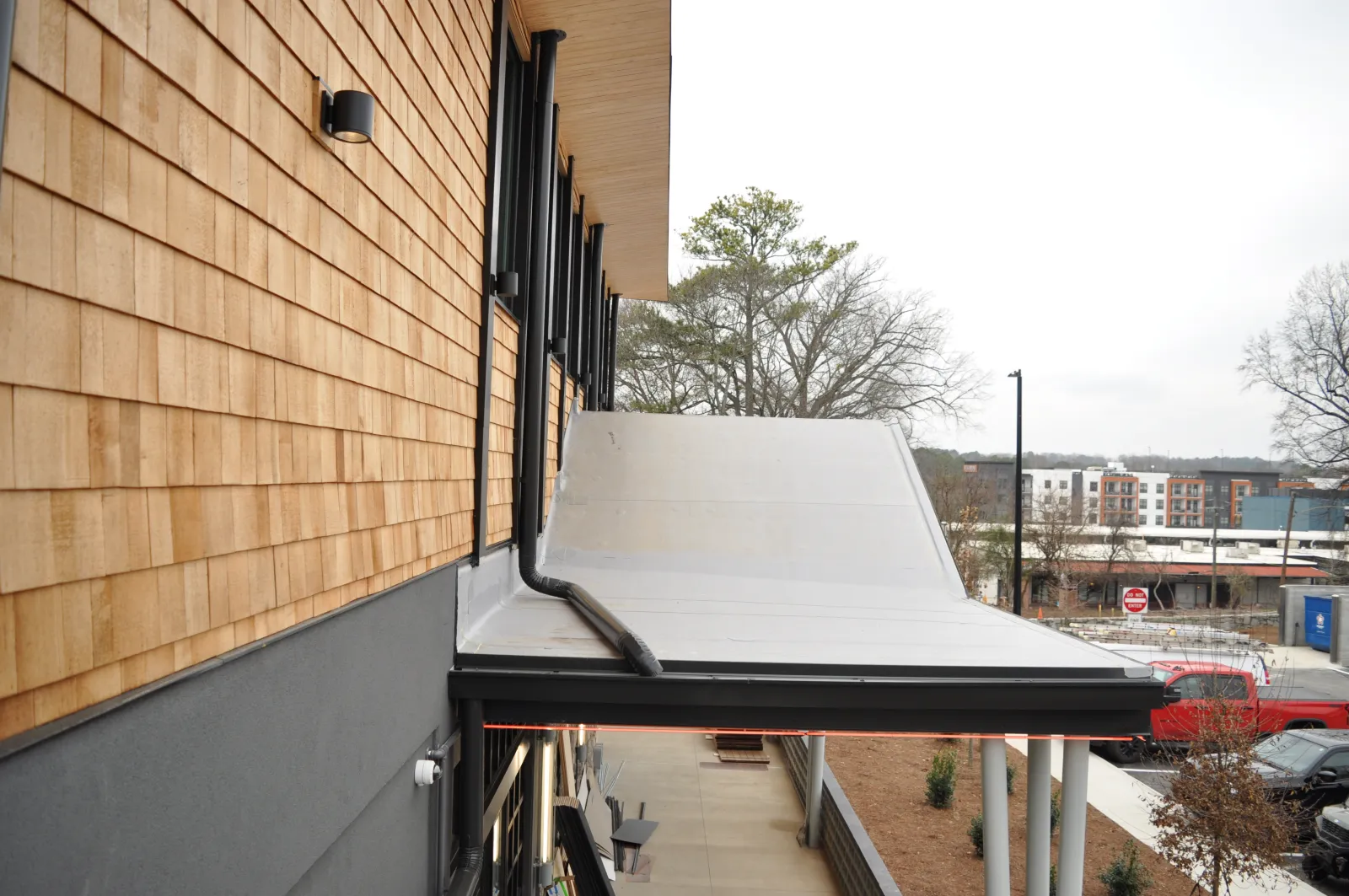 Modern building exterior with wooden siding, flat white roof, black gutters, and urban street view in background