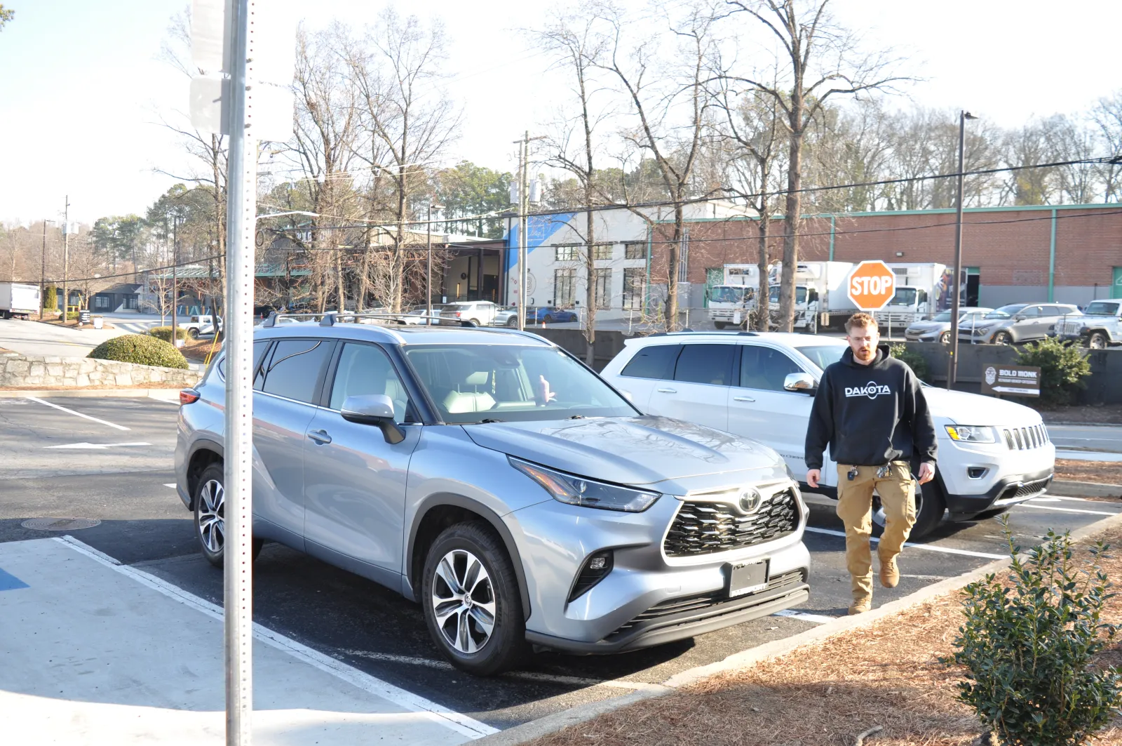 Man walking near silver Toyota SUV parked in outdoor lot with another white SUV and stop sign in background