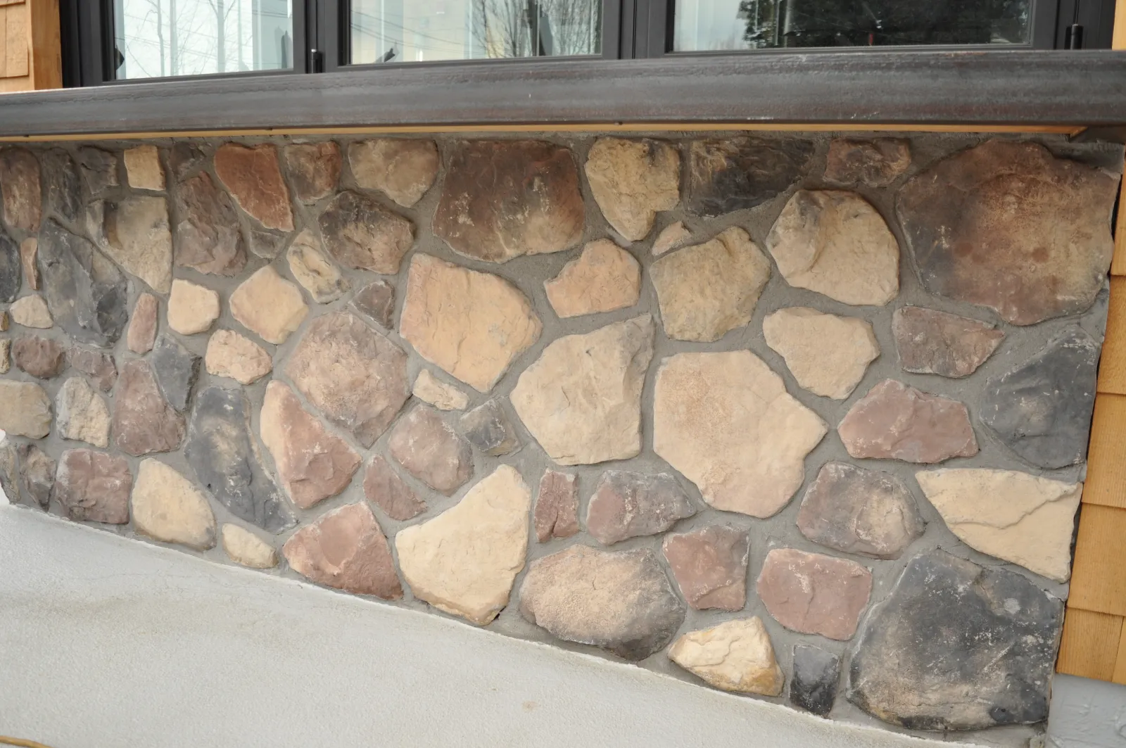 Rustic stone wall facade with various shades of brown and gray stones under a wooden ledge.