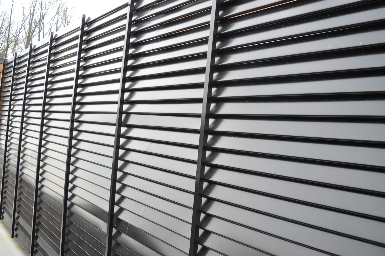 Black metal slatted fence with vertical supports creating a modern privacy barrier outdoors.