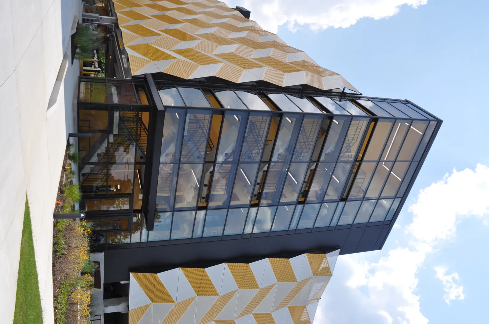 Modern building with geometric yellow and white facade panels and large glass windows under a blue sky.
