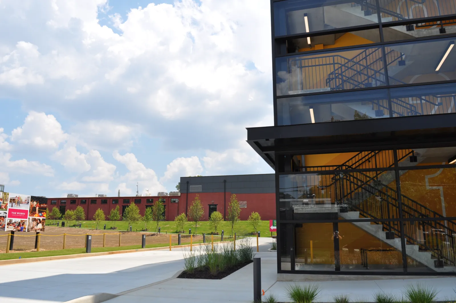 Modern building with glass windows and visible staircase next to a green lawn and partly cloudy sky.