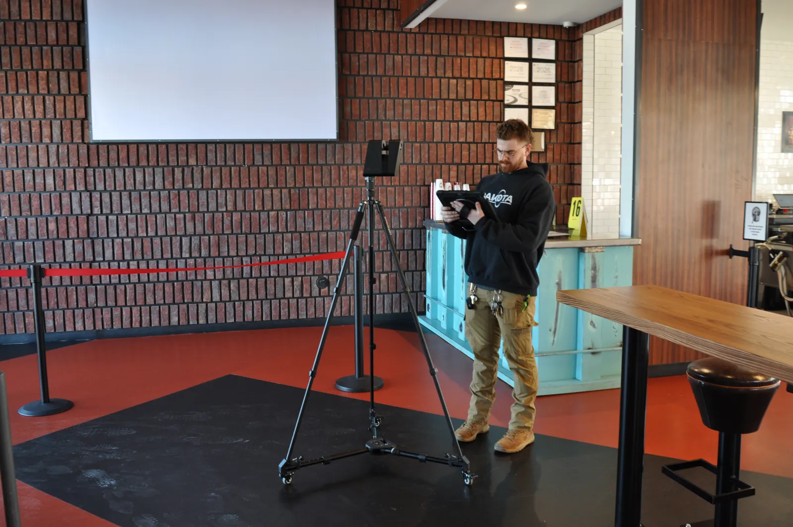 Man operating a camera on a tripod inside a modern industrial-style room with brick walls and wooden furniture