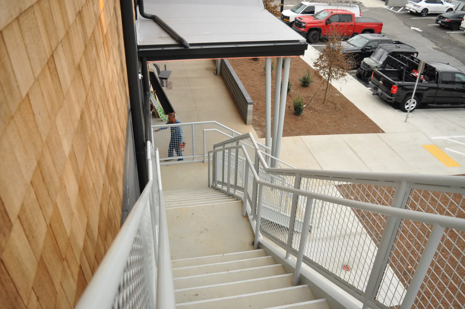 Outdoor concrete staircase with metal railing leading down beside wood-paneled building near parking lot with trucks.